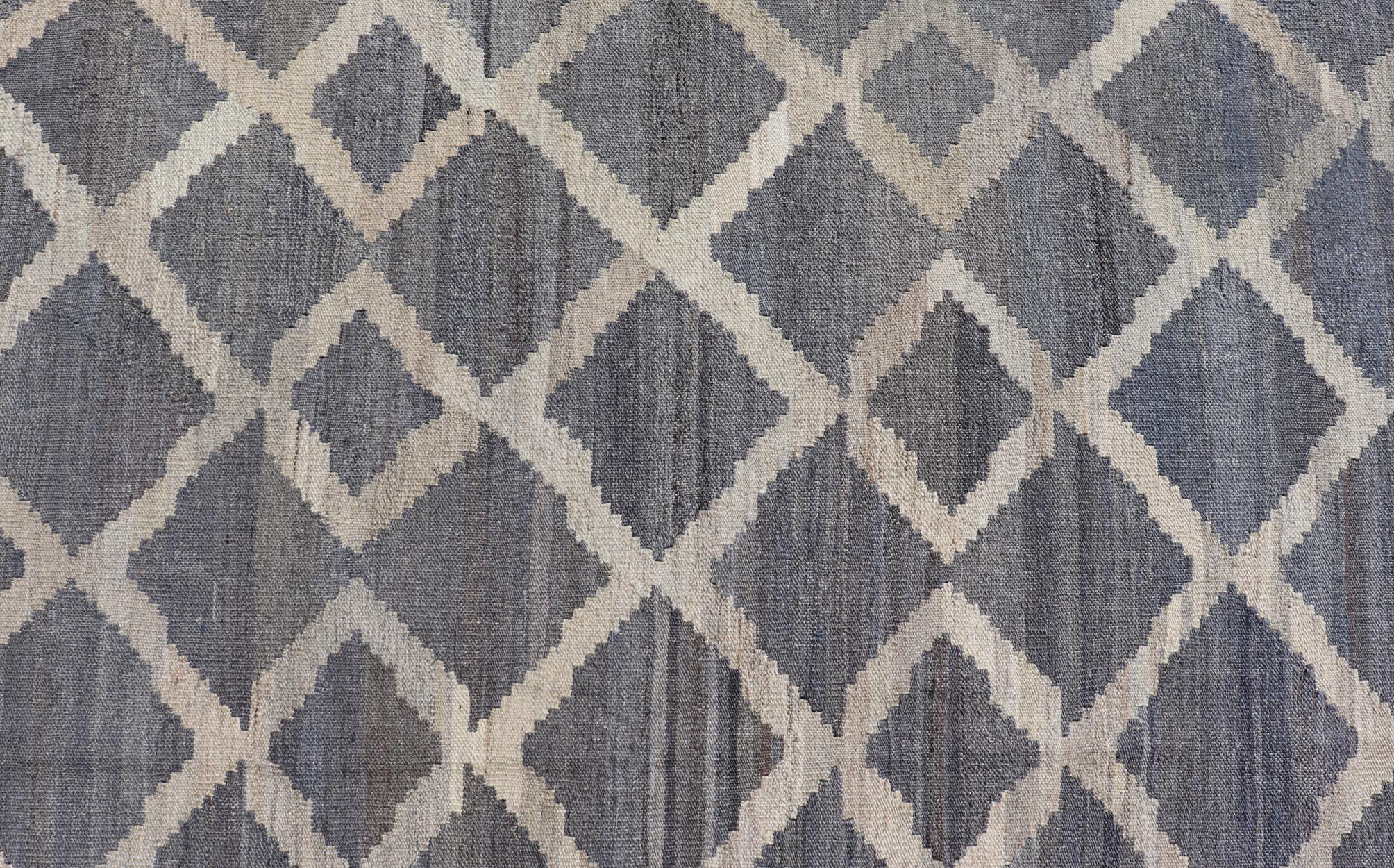 This modern flat-weave kilim has been hand-woven. The rug features a modern sub-geometric interlocked diamond design, rendered in blues, grays and cream; making this rug a superb fit for a variety of classic, modern, casual and minimalist