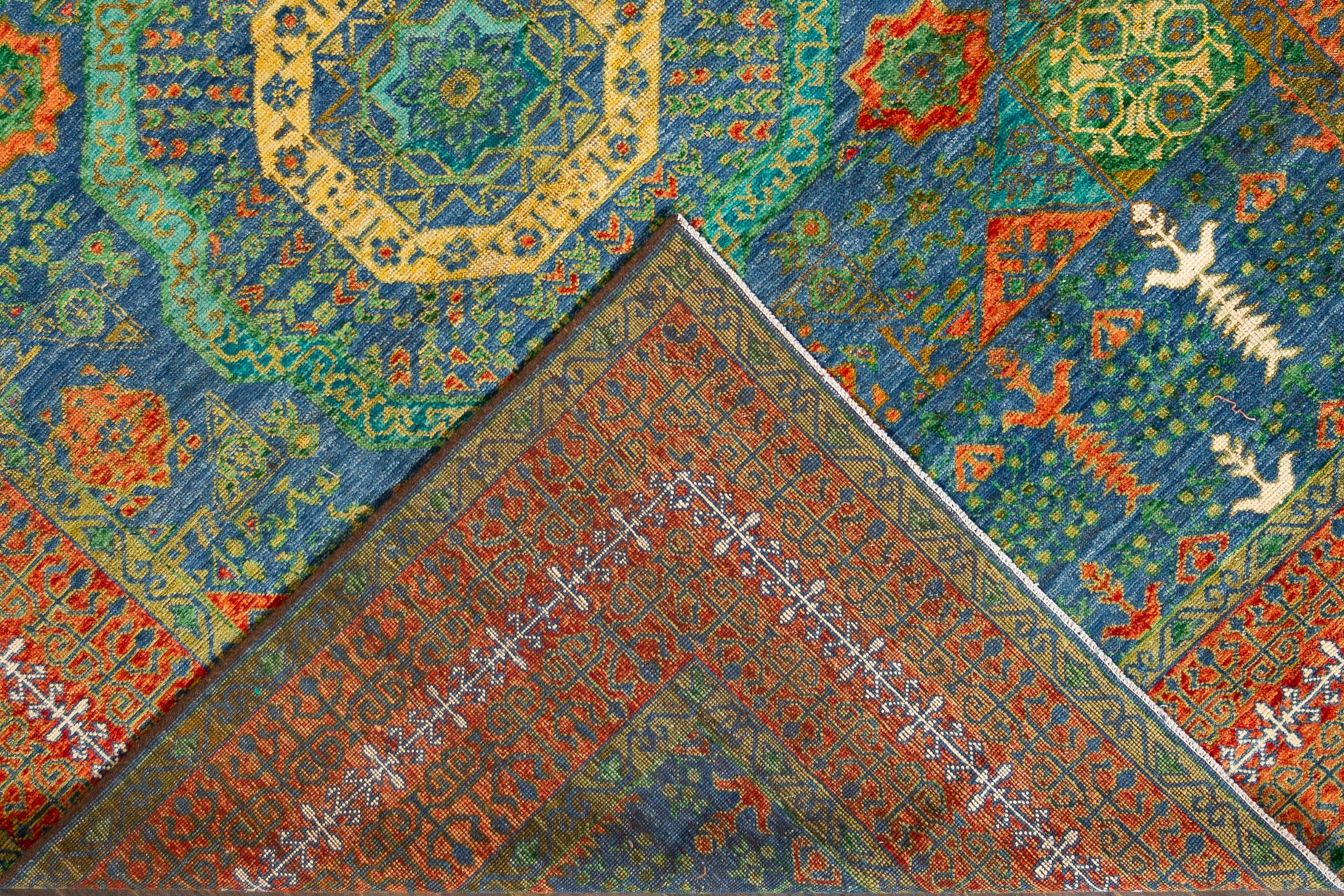 This stunning modern Mamluk hand-knotted wool rug is crafted from the finest quality wool. This exquisite piece showcases a deep blue field adorned with a rich rust frame and an intricate rosette design beautifully accented with hints of