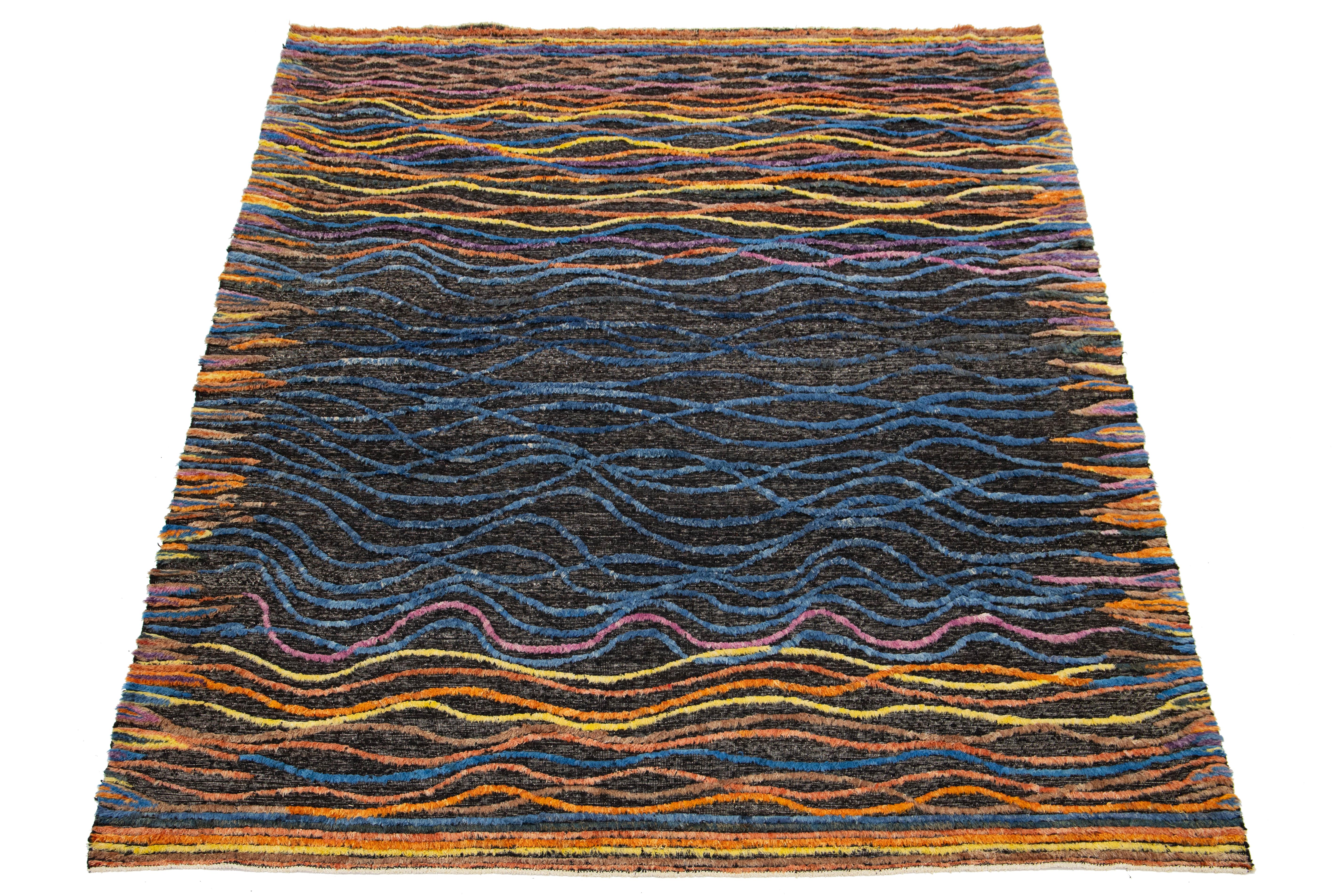 Presentamos esta impresionante alfombra de lana de estilo marroquí hecha a mano, que combina a la perfección el diseño contemporáneo con el arte tradicional. Con una vibrante mezcla de tonos naranjas, amarillos y azules, esta alfombra presenta