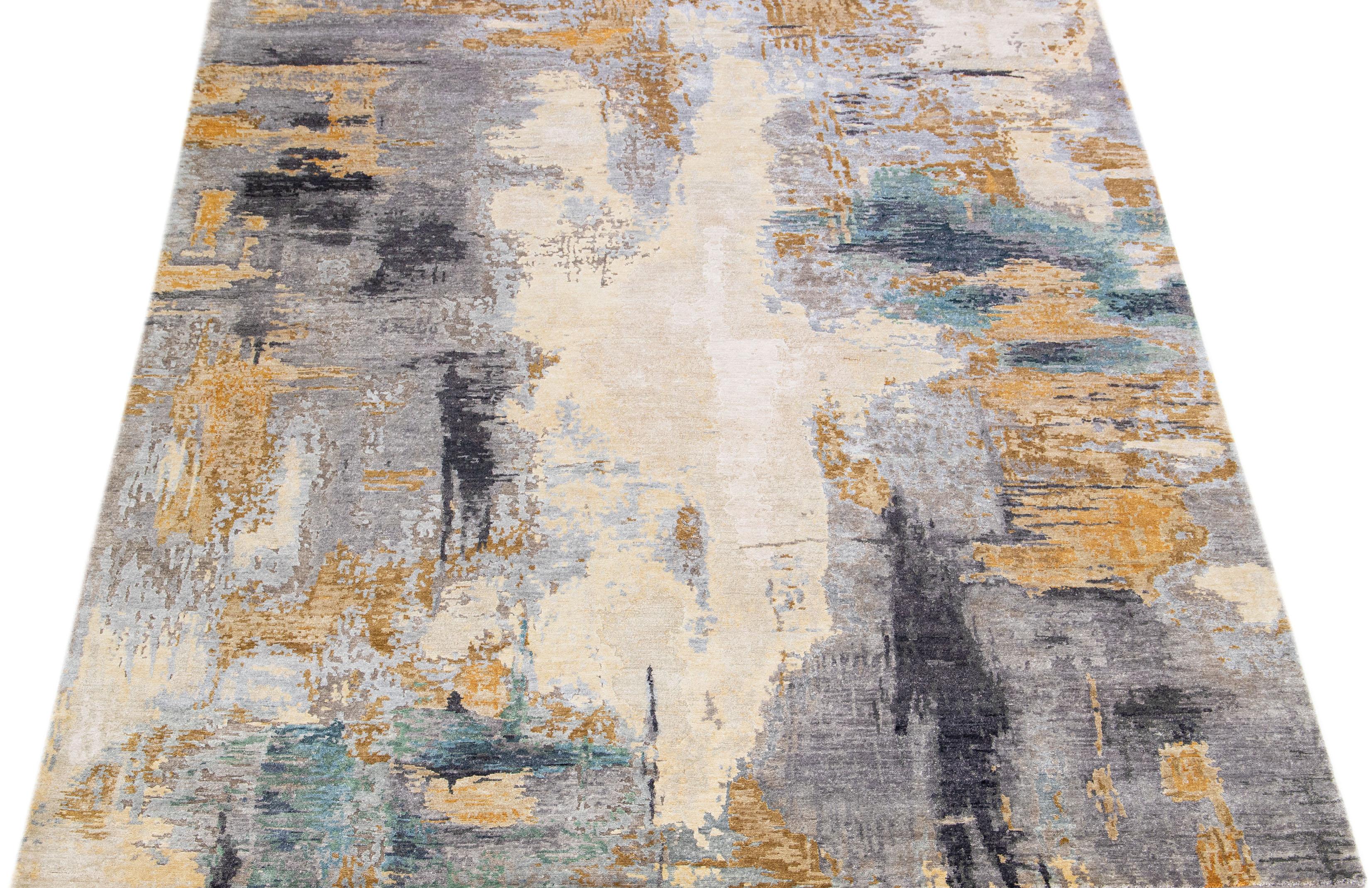 This wool and silk rug boasts a striking contemporary design featuring a beautiful motif in an elegant grey hue. The exquisite golden and ivory accents perfectly complement the distinct abstract pattern, lending an alluring touch of glamour that