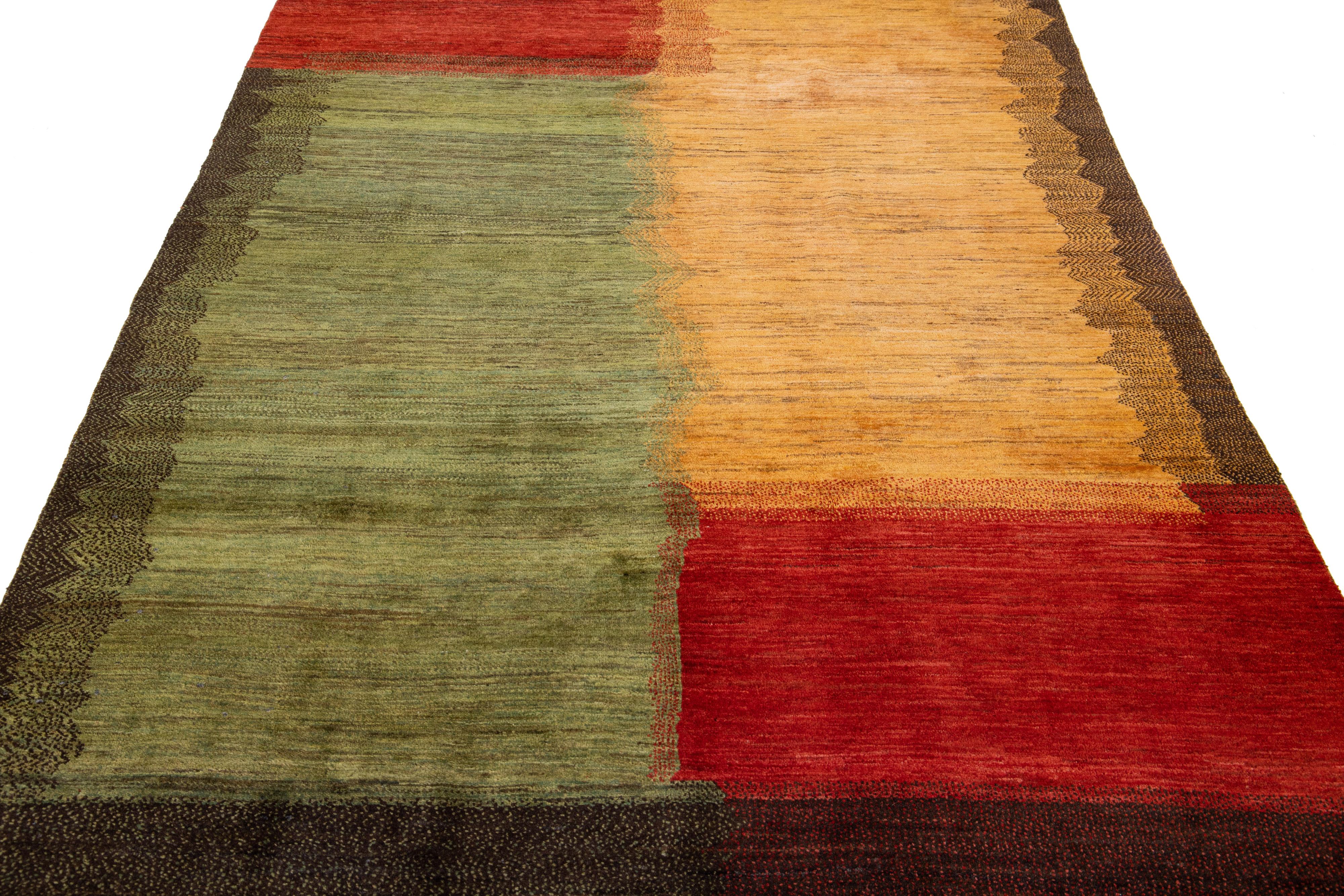 Beautiful modern Gabbeh-style hand-woven wool rug with a green, red, goldenrod, and brown color field and gorgeous abstract design.

This rug measures: 5'7