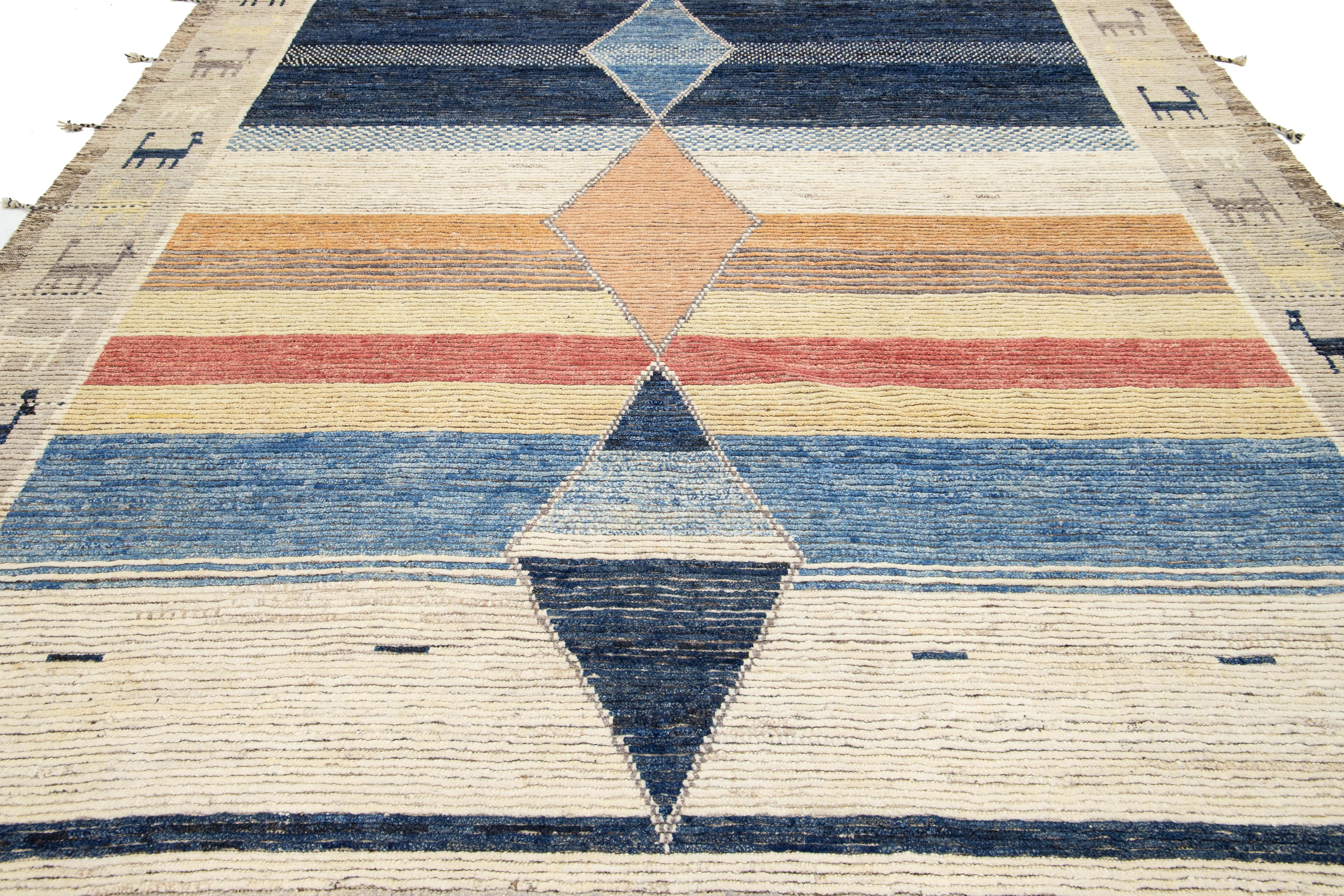 Esta alfombra artesanal contemporánea de lana de estilo marroquí. Con una armoniosa mezcla de tonos beige, azul y naranja, esta alfombra combina a la perfección la artesanía tradicional con el diseño moderno. Los intrincados motivos tribales realzan