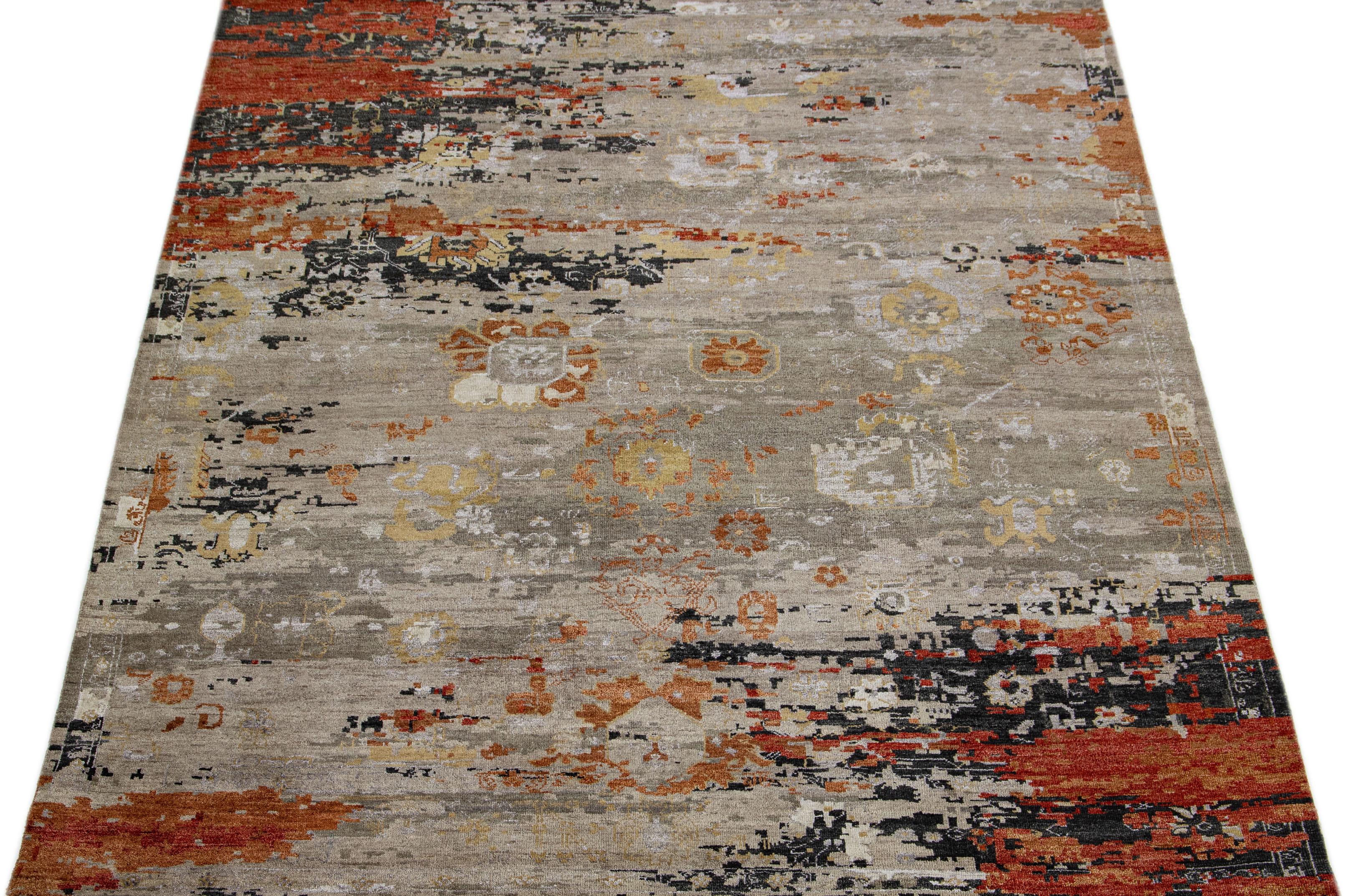 This wool and silk rug boasts a striking contemporary design featuring a beautiful motif in an elegant grey hue. The exquisite orange accents perfectly complement the distinct abstract pattern, lending an alluring touch of glamour that sets it