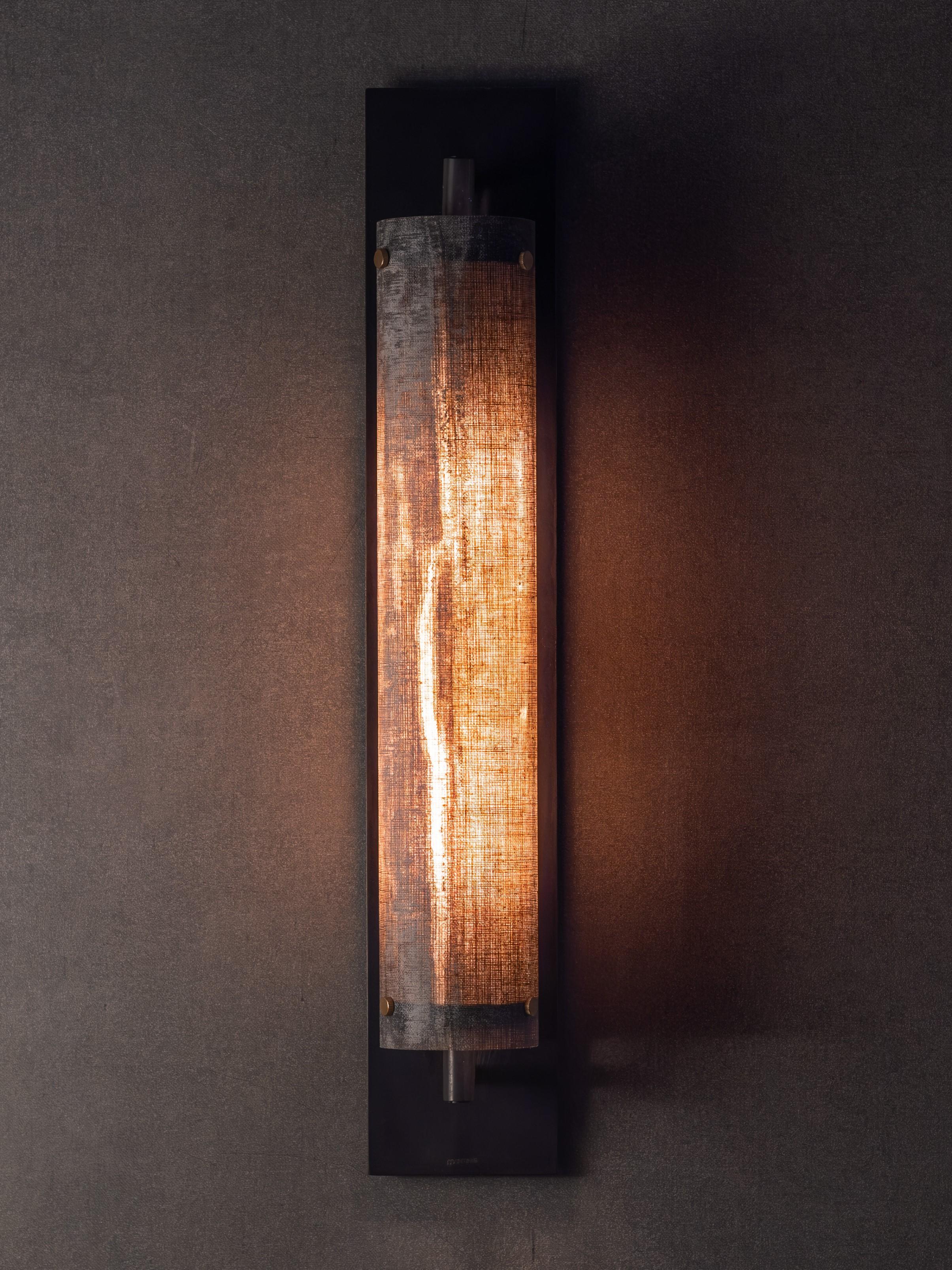 The Petra Pole Sconce is recognizable by our signature micarta shade, handmade from linen and resin. 
The lightweight shade produces a soft, ambient glow and visual interest lit and unlit.  The cylindrical 'pole' shade mounts onto a blackened brass