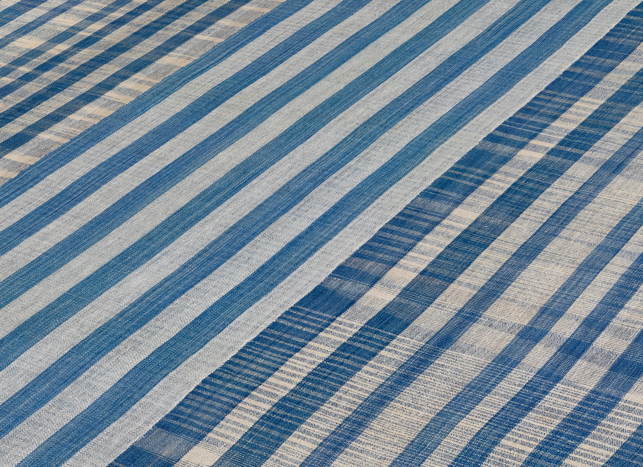 Ce tissage plat moderne, réalisé à la main en Iran, est composé à 100 % de laine naturelle non teintée, mettant en valeur l'habileté raffinée des artisans persans. Le design présente des nuances de bleu dans des motifs linéaires et à carreaux,