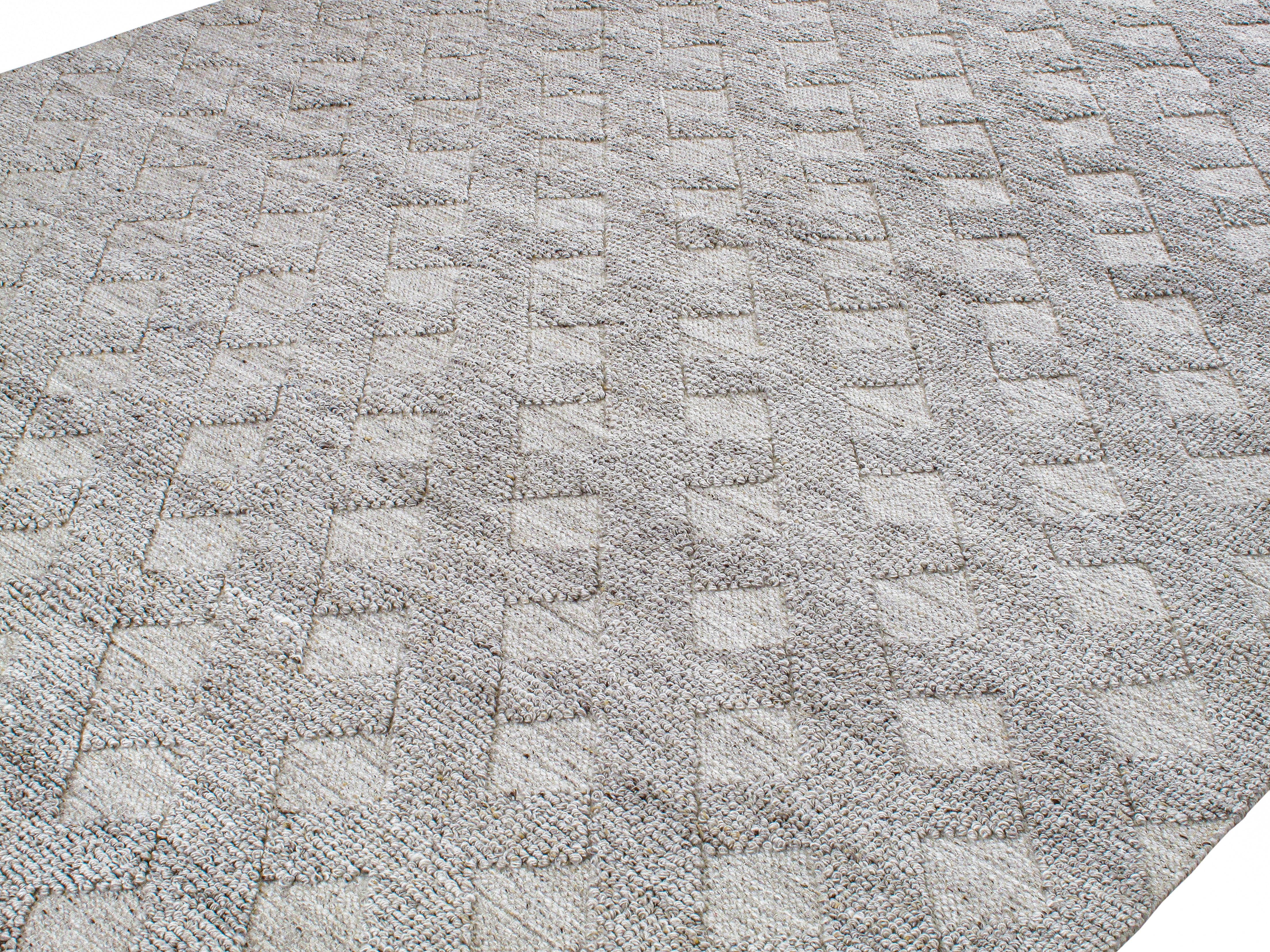 Dieser moderne Teppich wird in Indien aus hochwertiger neuseeländischer Merinowolle handgewebt, die wegen ihrer Weichheit, Langlebigkeit und edlen Oberfläche ausgewählt wurde. Die Palette besteht aus natürlich neutraler Wolle, frei von synthetischen