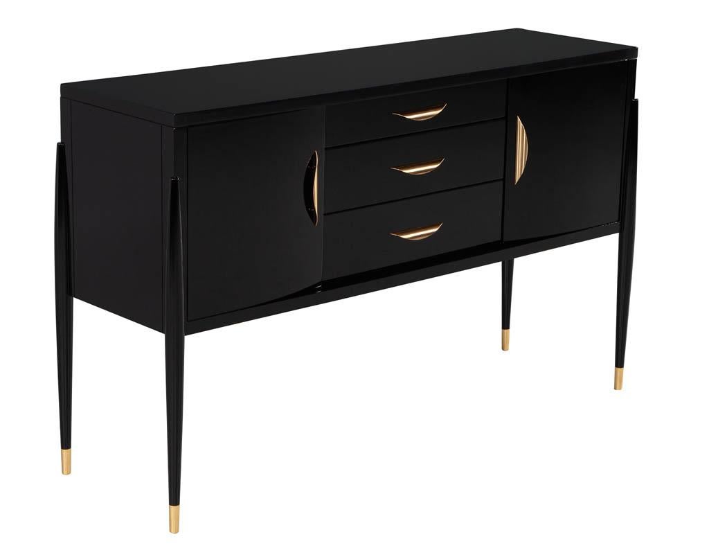 Modern High Gloss Black Lacquer Sideboard. New from the USA, this creation is a mixture of modern styling with a traditional soul. Beautiful sleek curved door panels with unique rounded legs tapering to metal sabot in brass. Completed with a high