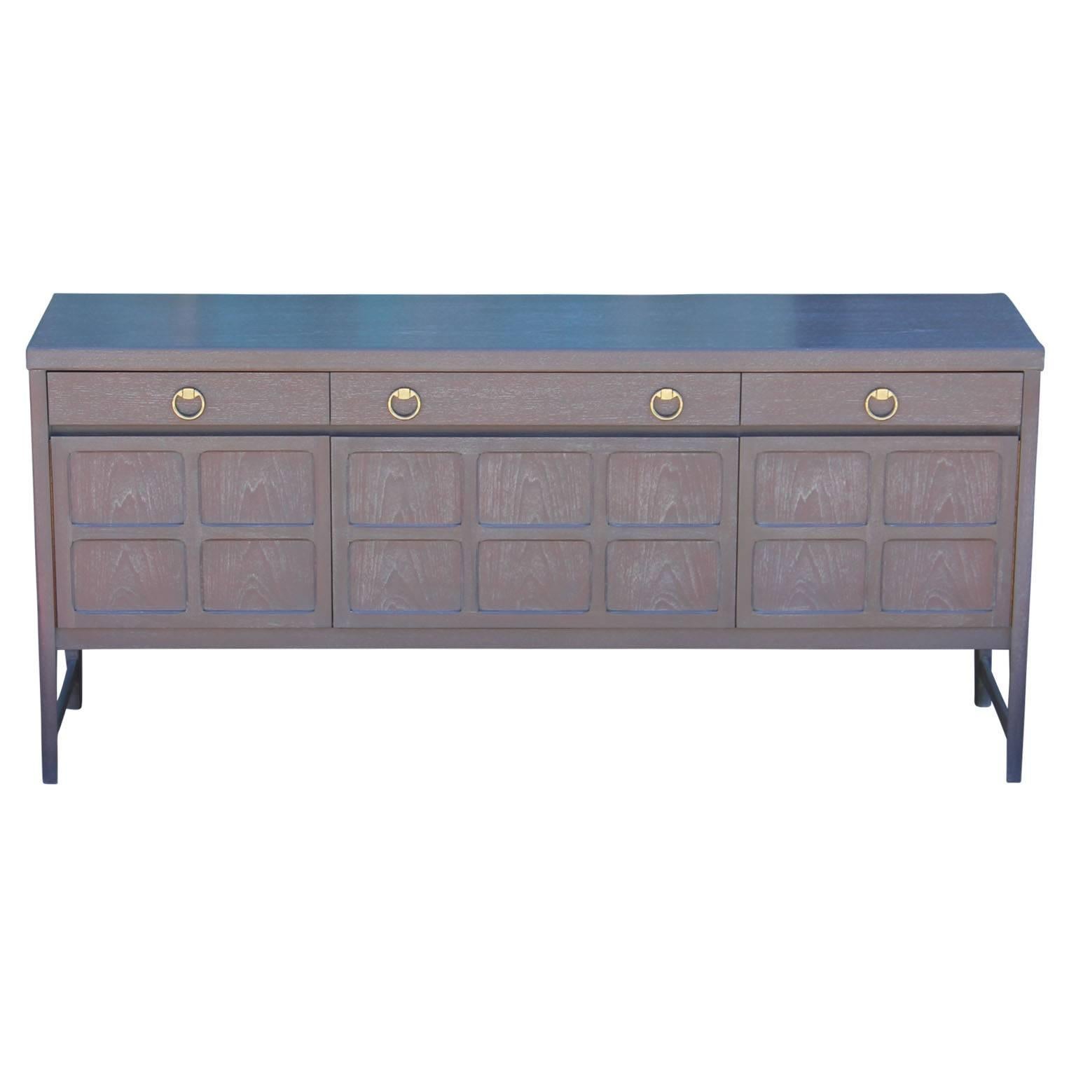 Wonderful modern / Hollywood Regency style sideboard with a grey cerused finish and outfitted with brass ring handles.  This credenza features three drawers at the top; one with dividers, making it easy to keep organized and shelving on the bottom.
