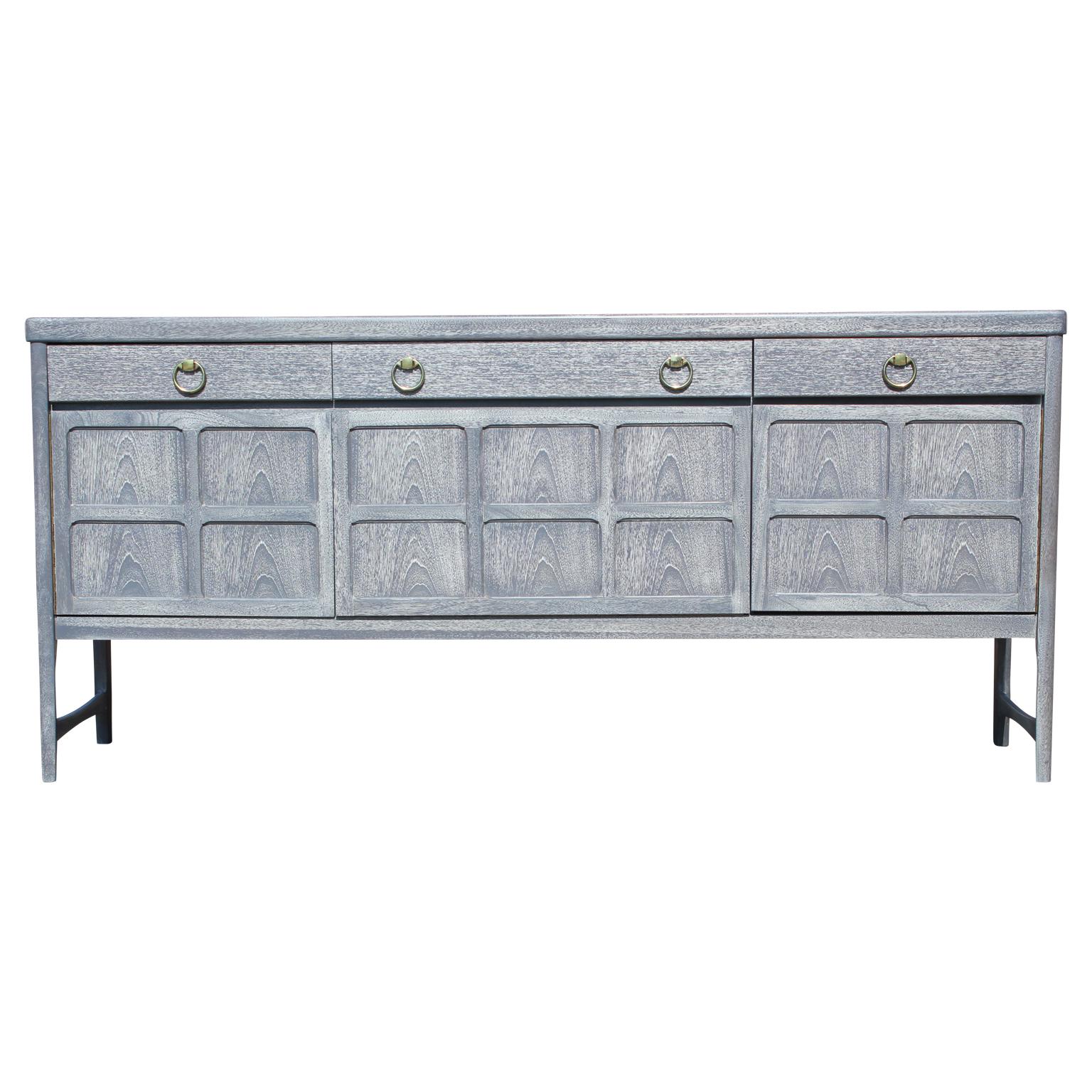 Wonderful modern / Hollywood Regency style sideboard with a grey cerused finish and outfitted with brass ring handles. This credenza features three drawers at the top; one with dividers, making it easy to keep organized and shelving on the bottom.
