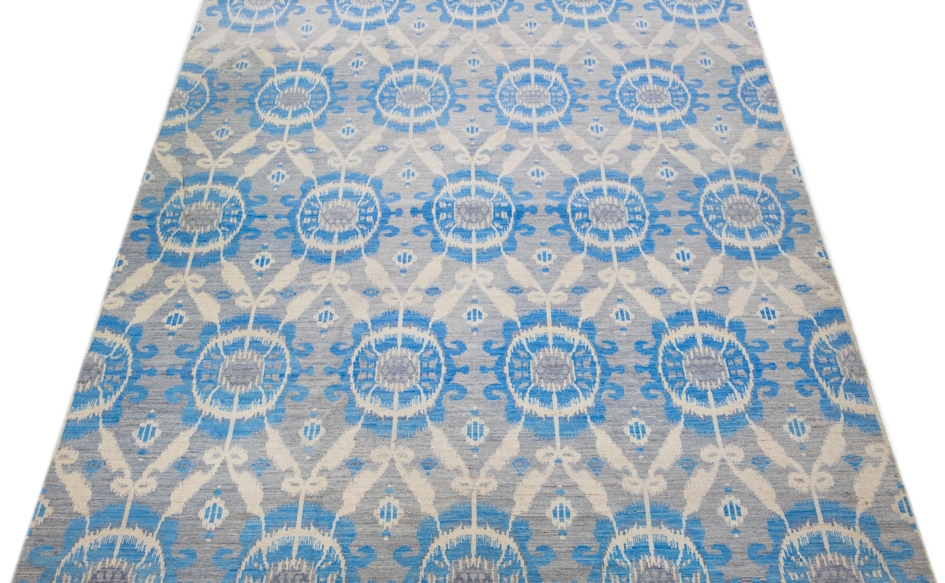 Dieser atemberaubende Ikat-Teppich ist aus Wolle handgeknüpft und zeichnet sich durch ein stilvolles graues Farbfeld aus. Das geometrische Allover-Muster wird durch elegante Blau- und Beigetöne akzentuiert und ist eine wunderbare Ergänzung für jeden