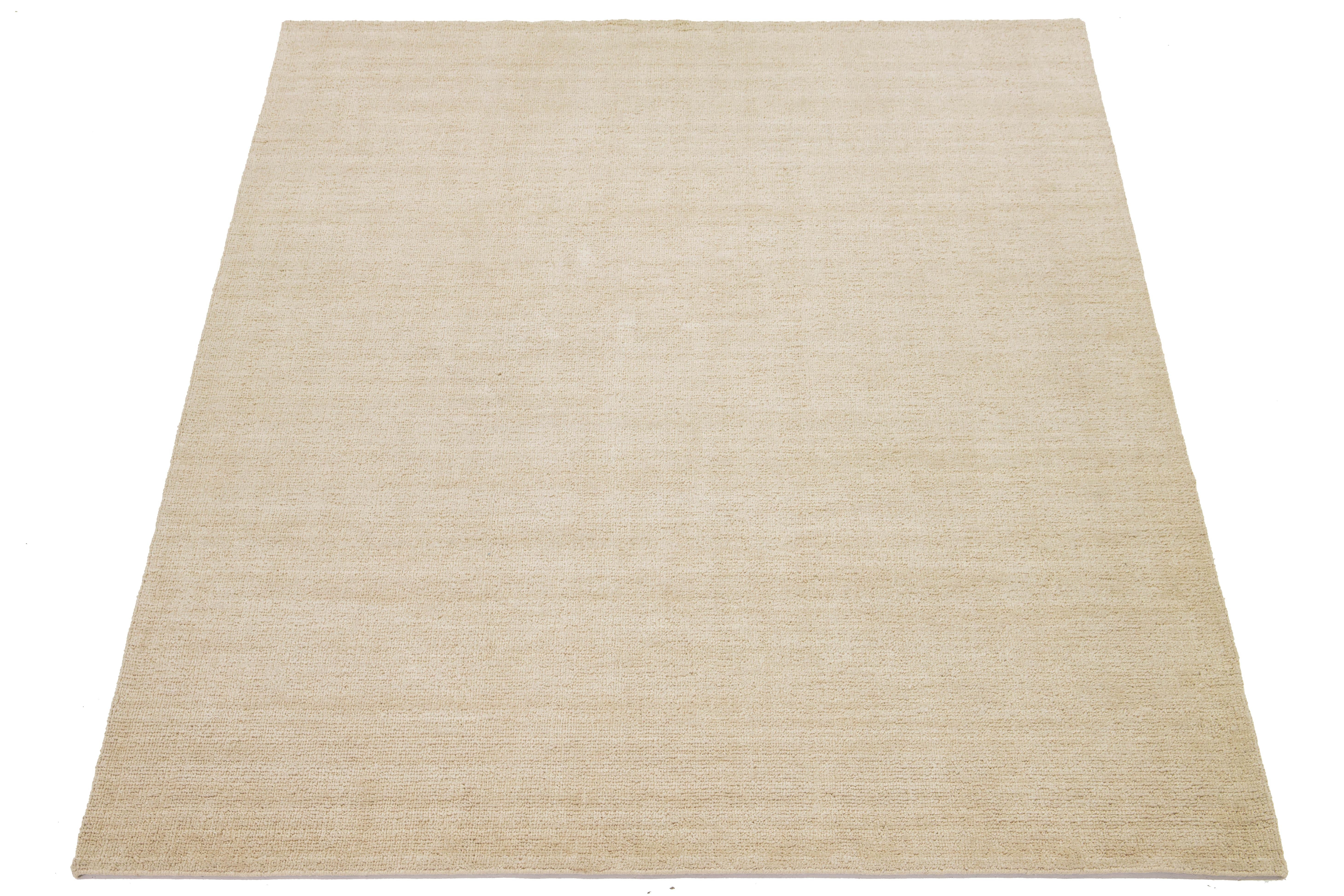 Ce tapis indien moderne en laine nouée à la main est habilement tissé par des artisans et présente un design solide. Sa douce teinte beige sert de toile de fond polyvalente, ce qui lui permet de se fondre harmonieusement dans différents styles
