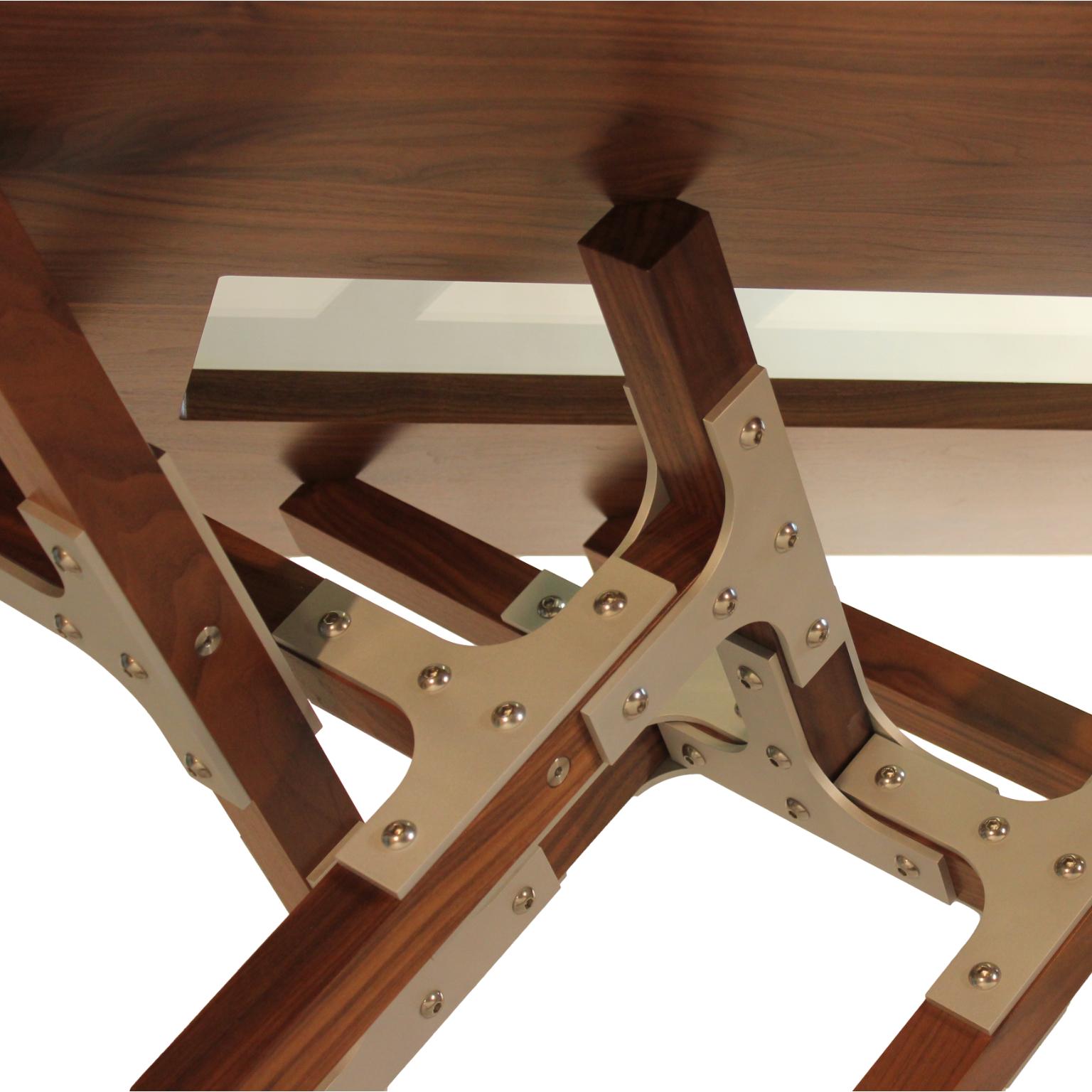 The Saratoga dining table by Peter Harrison has a dynamic base made from walnut squares and aluminum brackets. The design is almost crystalline as it radiates up to support the walnut top. There is a tempered glass window through the top to view the