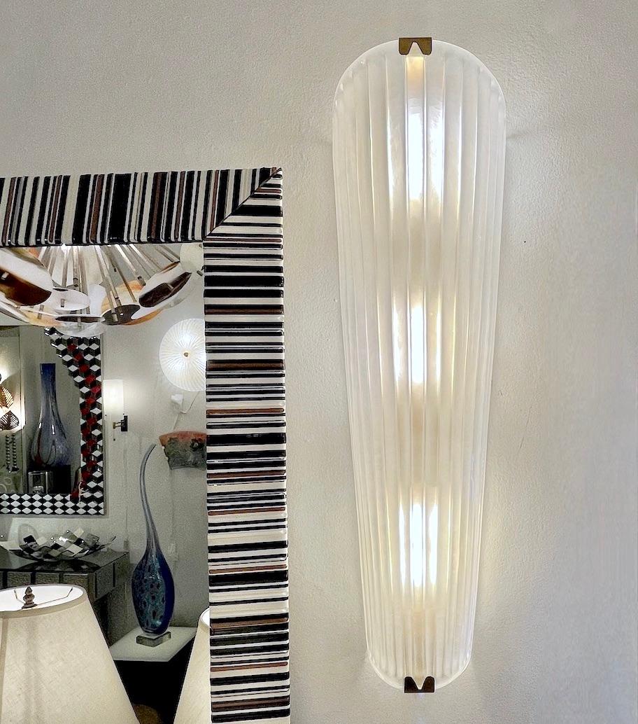 Un par de monumentales apliques geométricos altos de color blanco esmerilado iridiscente, de elegante forma cónica, fabricados totalmente a mano en Italia, en cristal soplado de Murano texturizado con motivos acanalados Art Decó, sobre un marco de