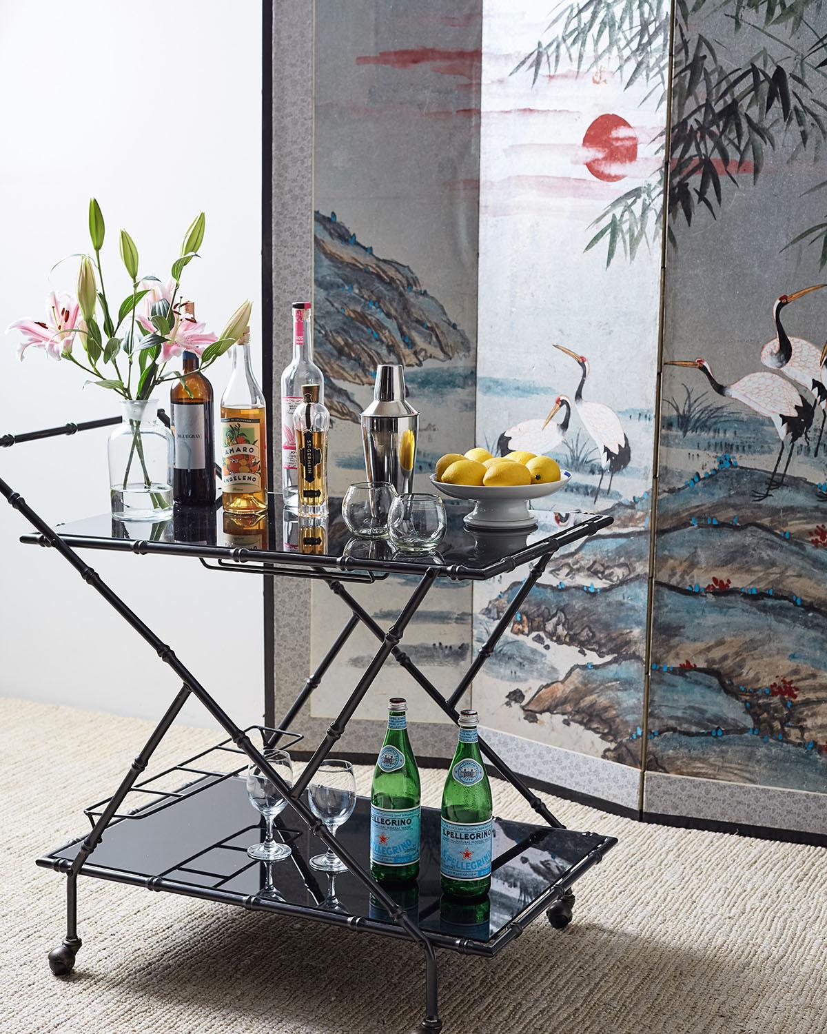 Chic Italian rolling bar cart having a black anodized metal faux bamboo frame. Hollywood Regency design with a modern twist. Constructed with two tiers inset with black tempered glass, the bottom tier having a bottle caddy. High quality design and