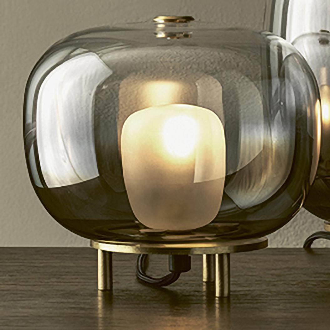 Mini table lamp with lampshade in borosilicate glass and frame in Natural Brass. This table lamp is part of a lighting project comprehending pendant glass balls floating in the air, making spectacular lighting effects. The lampshade is available in