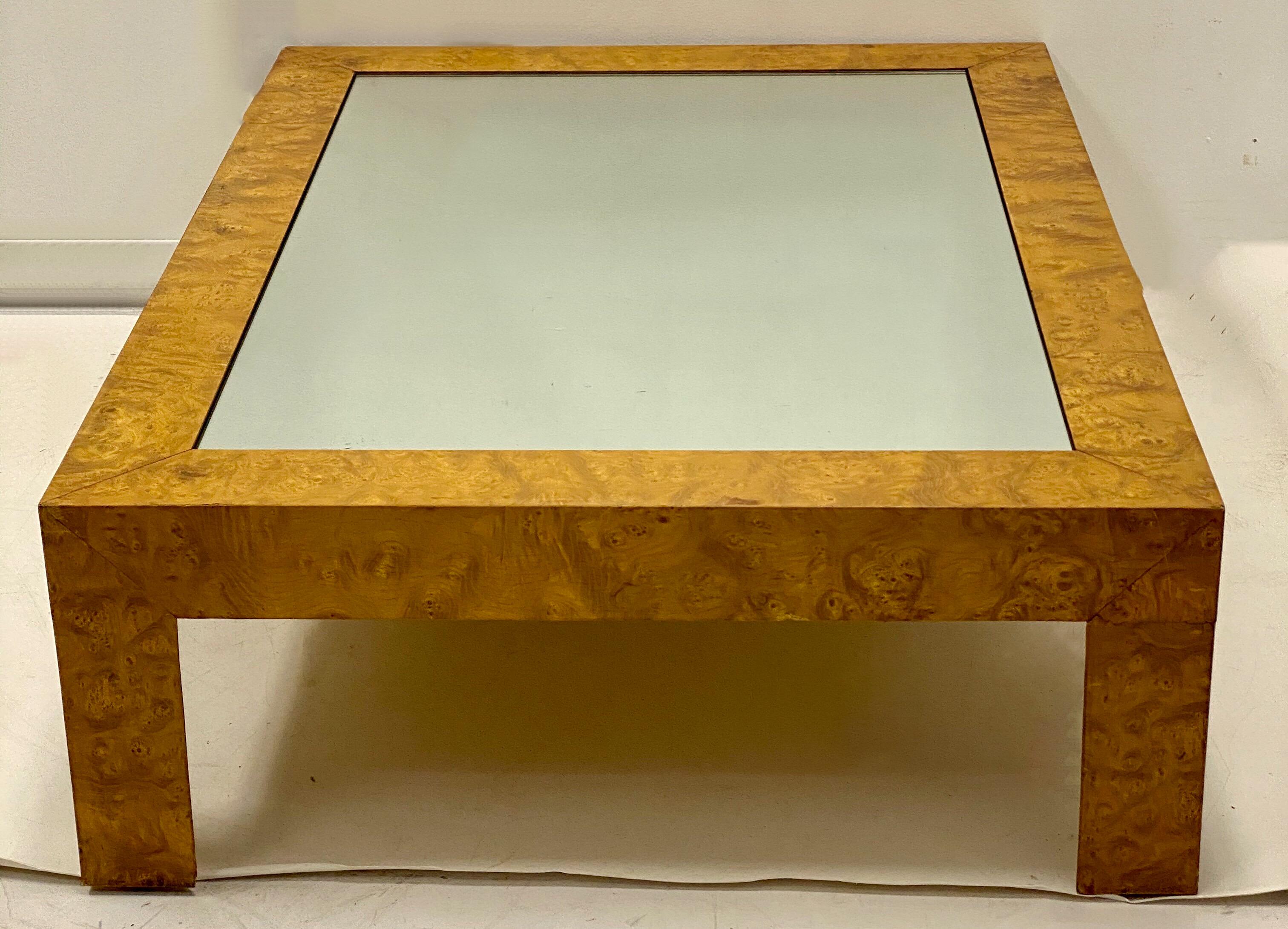 This is a Mid-Century Modern burlwood coffee table with mirror glass insert. It is done in the manner of Milo Baughman. It most likely dates to the 70s and is in very good condition.