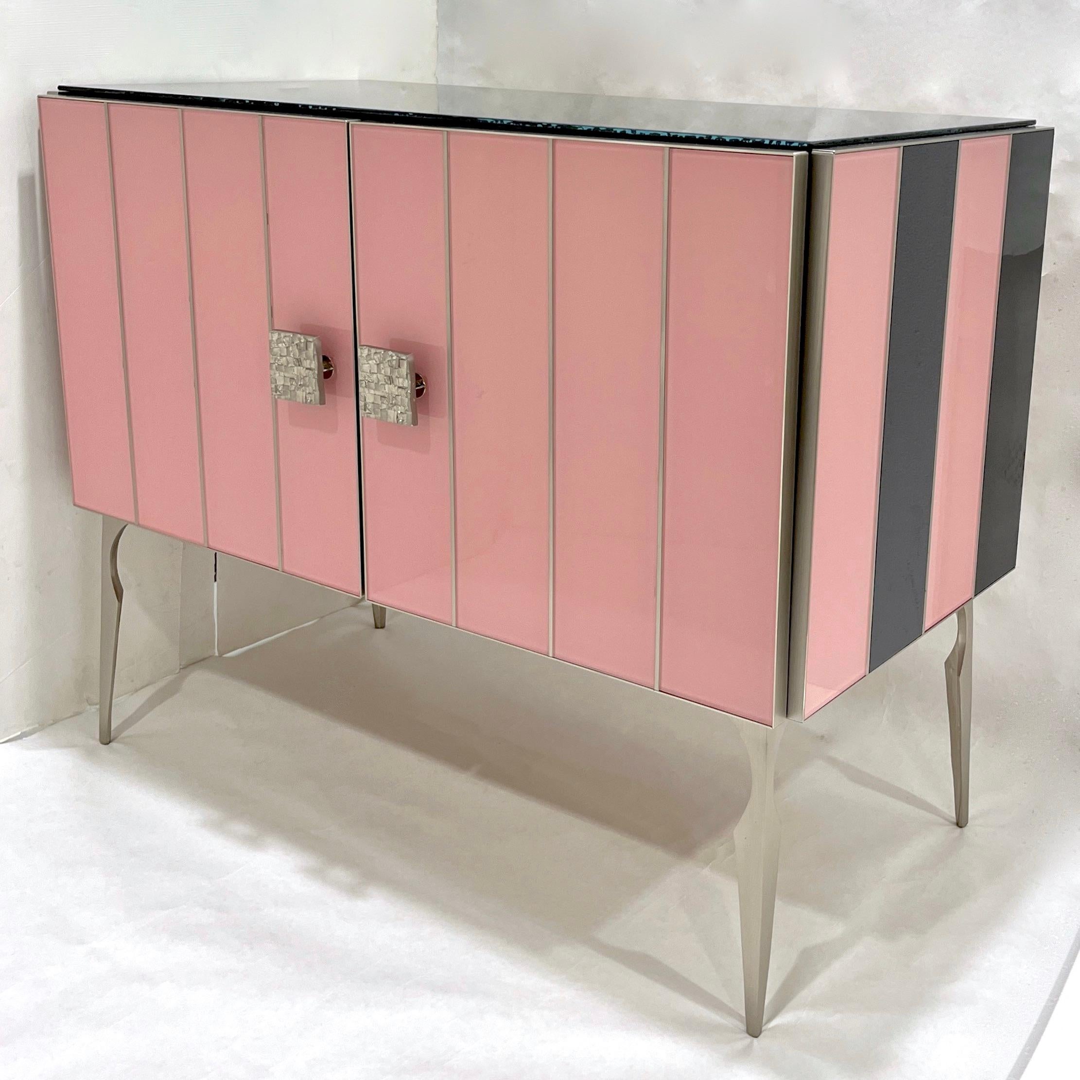 Apportez du glamour à votre pièce avec cette armoire moderne personnalisable sur mesure, entièrement fabriquée à la main en Italie, au style Hollywood Regency. L'entourage est décoré de verre d'art d'un rose saumoné doux saisissant et d'un noir de