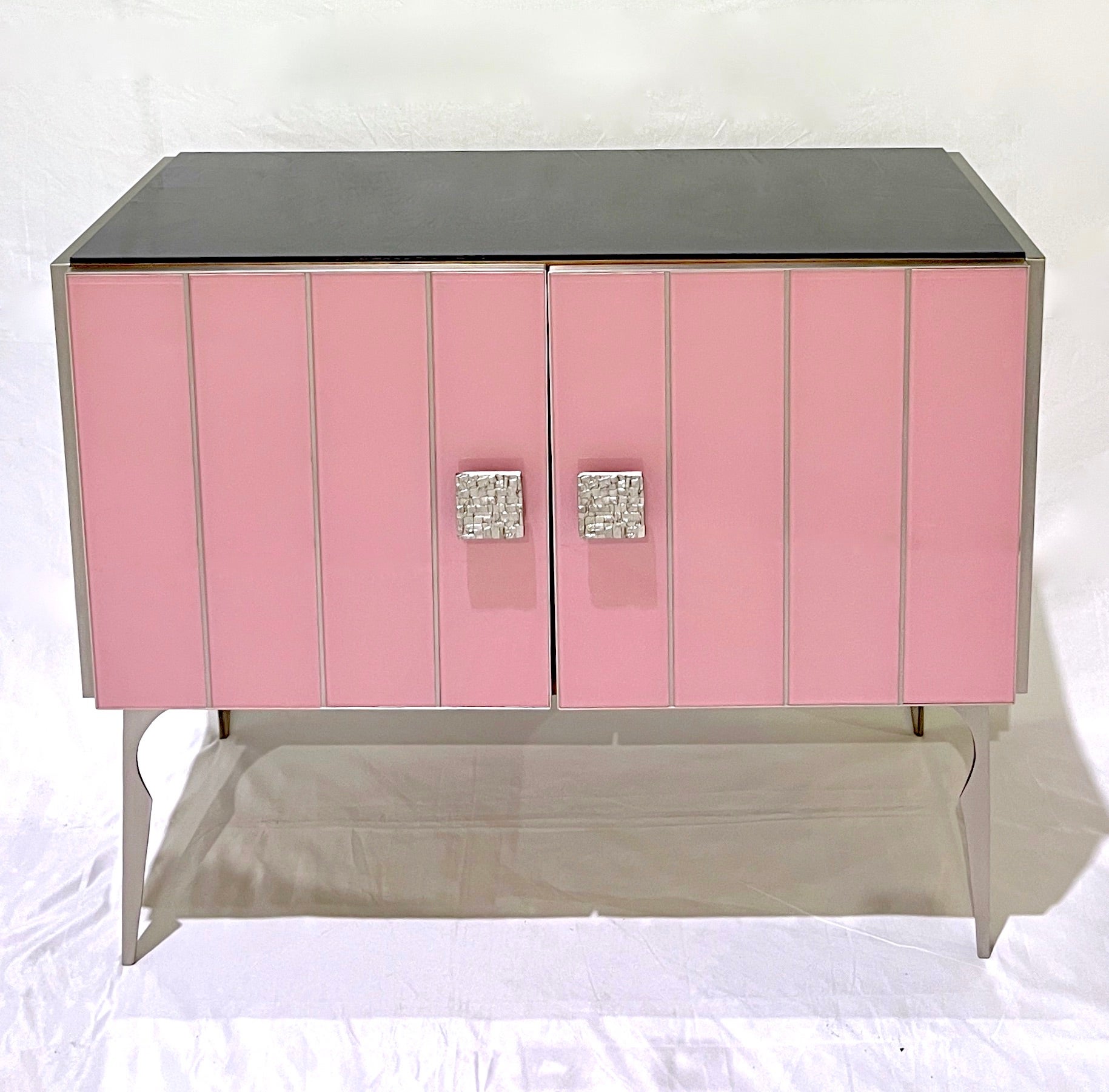 Apportez du glamour à votre pièce avec cette armoire moderne personnalisable sur mesure, entièrement fabriquée à la main en Italie, au style Hollywood Regency. L'entourage est décoré de verre d'art d'un rose saumoné doux saisissant, rayé