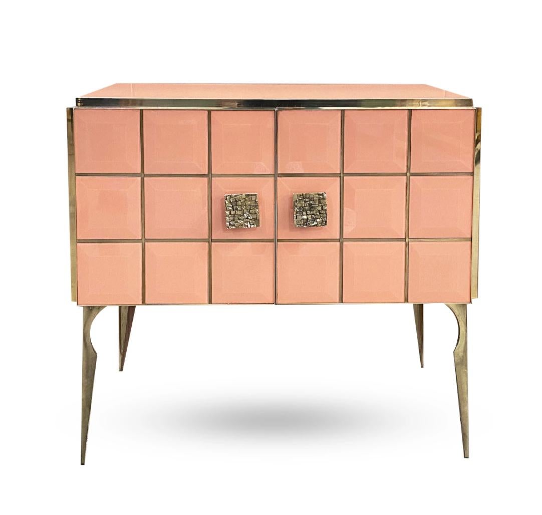 Faites entrer le glamour dans votre pièce avec ce meuble moderne sur mesure et personnalisable, entièrement fabriqué à la main en Italie, avec un aspect Hollywood Regency. L'entourage est décoré de verre d'art d'une couleur rose saumon brillante et