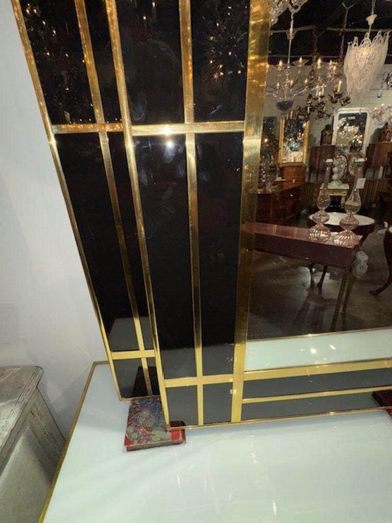 Ce miroir design italien moderne présente un cadre en verre noir épuré avec des accents en laiton poli, ajoutant une touche de luxe à n'importe quel espace. Parfait pour ajouter une touche sophistiquée à votre intérieur, ce miroir associe des