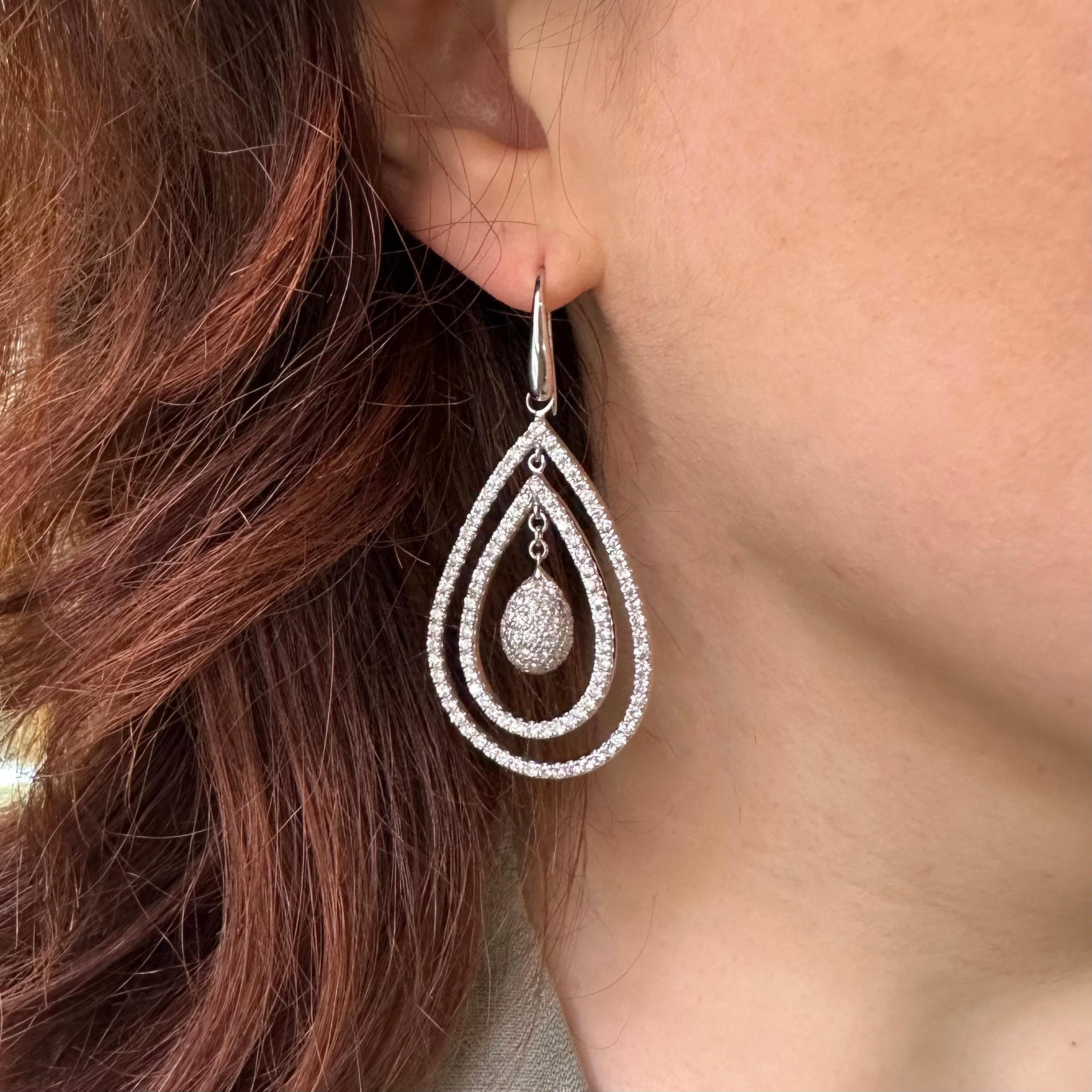 A pair of modern Italian drop shape earrings with polished tear drop shaped tops, onto wires, with two rows of round brilliant-cut diamonds, in claw settings, surrounding a pavé set diamond three dimensional drop, hanging from chain links, mounted
