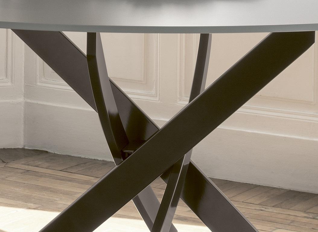 Dieser von Pocci&Dondoli entworfene Tisch zeichnet sich durch eine harmonische Drehung der geschwungenen Bögen aus, die seine einzigartige Basis umreißen. Die runde Platte besteht aus mattiertem, hellgrauem, kratzfest lackiertem Samtglas. Die matte