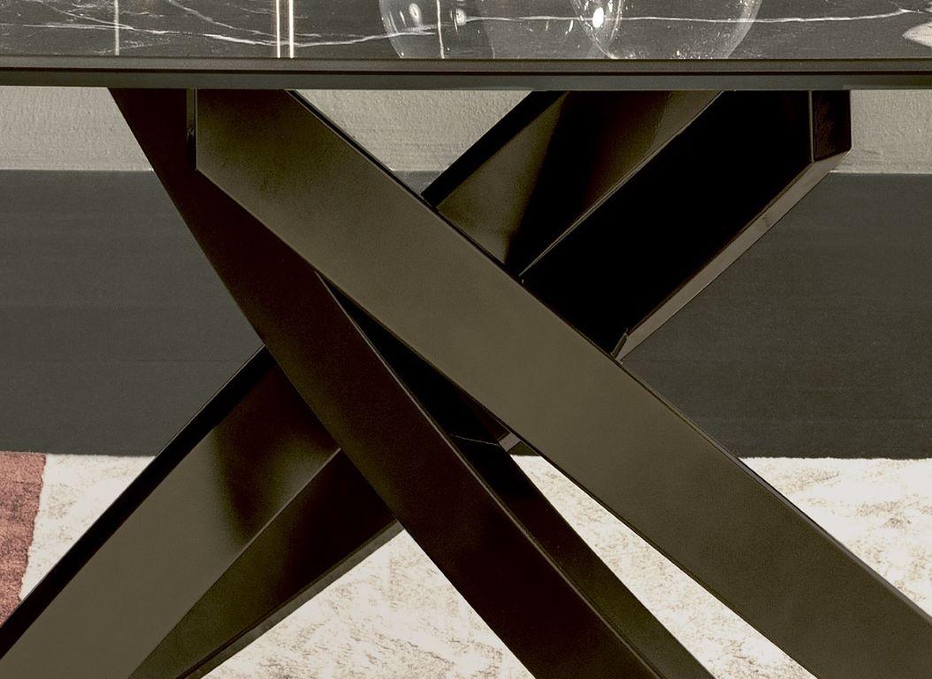 Der von Pocci&Dondoli entworfene feste Tisch hat eine tonnenförmige Platte aus Supermarmor und ein Gestell aus dunkelmessingfarben lackiertem Metall. Die von einer alten Schmiedemaschine gefertigte Schwerterkette ist der opulente Unterbau für ein