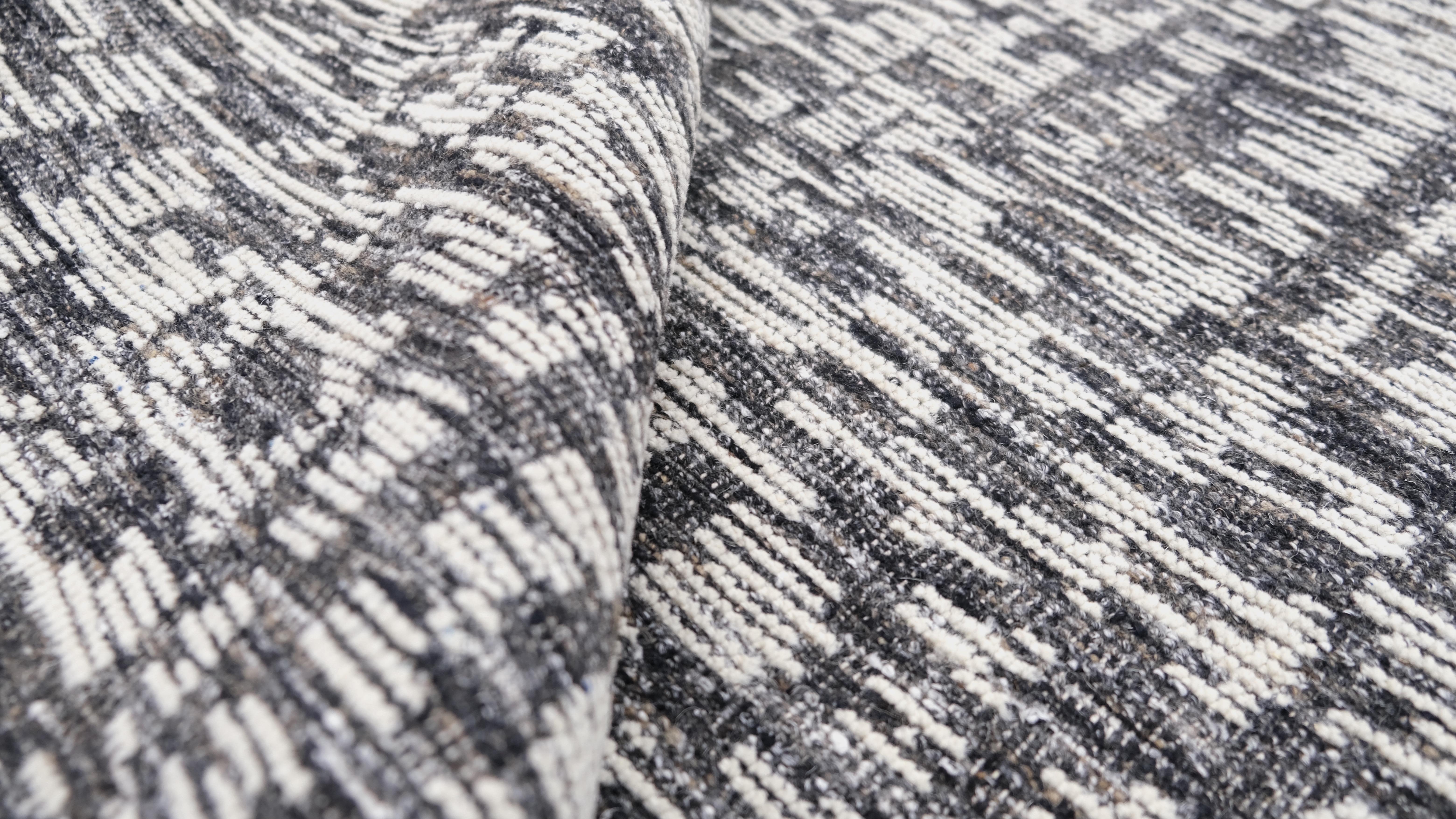 Verschönern Sie Ihren Wohnbereich mit diesem handgeknüpften Wollteppich in einem raffinierten, modernen Design. Das komplizierte, strukturierte Muster dieses Teppichs in Grau- und Elfenbeintönen erzeugt einen dynamischen visuellen Effekt, der ideal