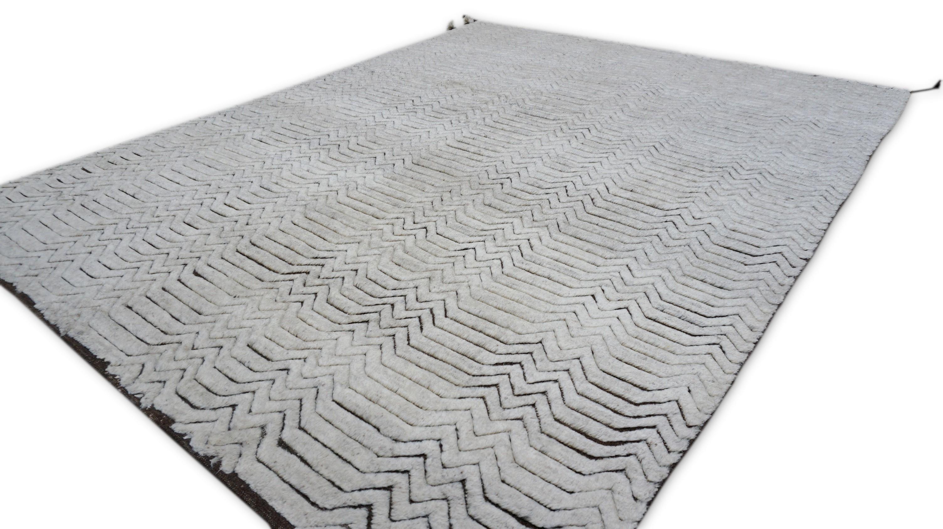 Dieser handgeknüpfte Wollteppich ist ein Beispiel für die Verbindung von modernem Design und handwerklicher Kunstfertigkeit: Er zeichnet sich durch ein präzises Chevron-Motiv aus feinen, gestaffelten schwarzen Linien auf einem weichen