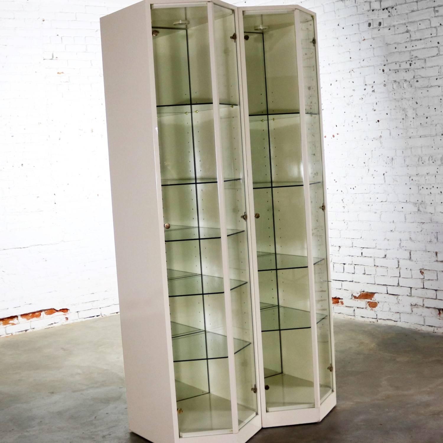 Extraordinary pair of modern ivory colored lacquer lighted full-view display cabinets with V shaped glass fronts and mirrored backs. Possibly Italian made, they are in wonderful vintage condition. There are small nicks to the very bottom of the base