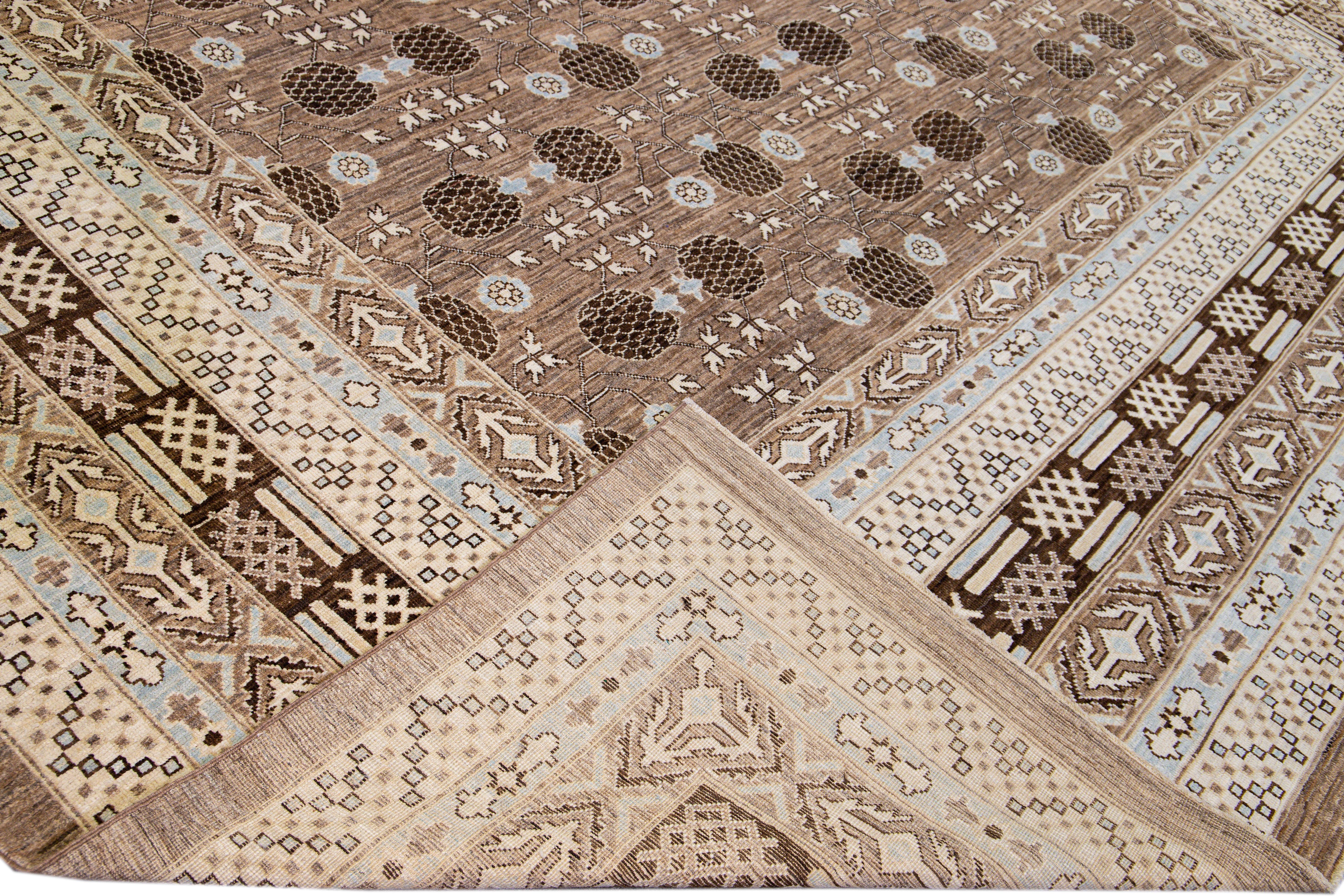 Beautiful modern oversize Khotan style rug from Pakistan with a brown field. This rug has a designed frame with blue, beige, and brown accents in interconnected pomegranates rosettes, leaves, and vines design. 

This rug measures 12'3