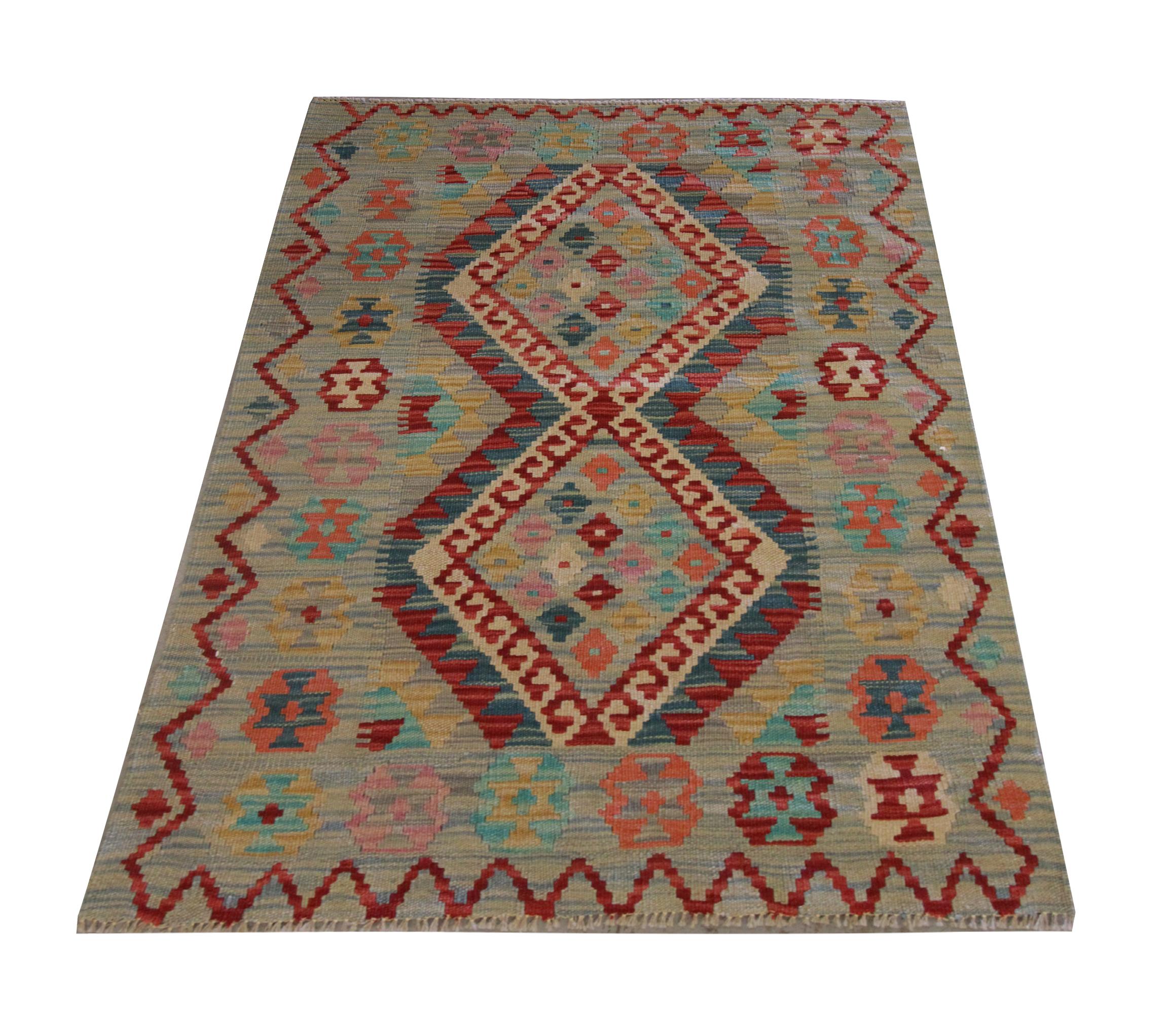 This fine wool area rug is a handwoven Afghan kilim constructed in the early 21st century. Radiant colours make up the two medallions in the centre, featuring blue, red, green and cream on a subtle grey-blue background. This has then been framed by