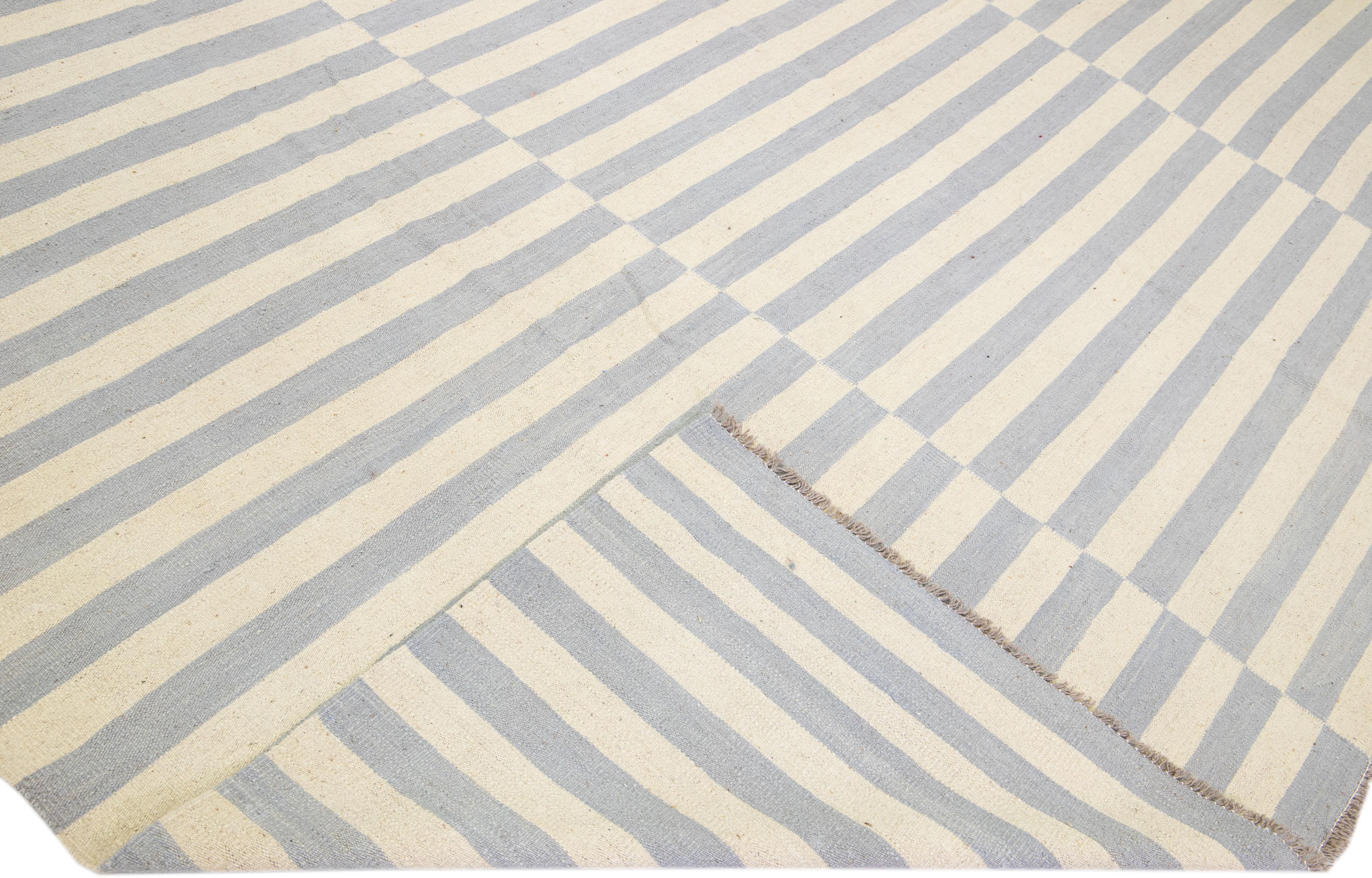 Beautiful Modern flat-weave Kilim handmade wool rug with a beige color field. This Kilim rug has gray accents in a gorgeous all-over stripe design.

This rug measures: 12'5
