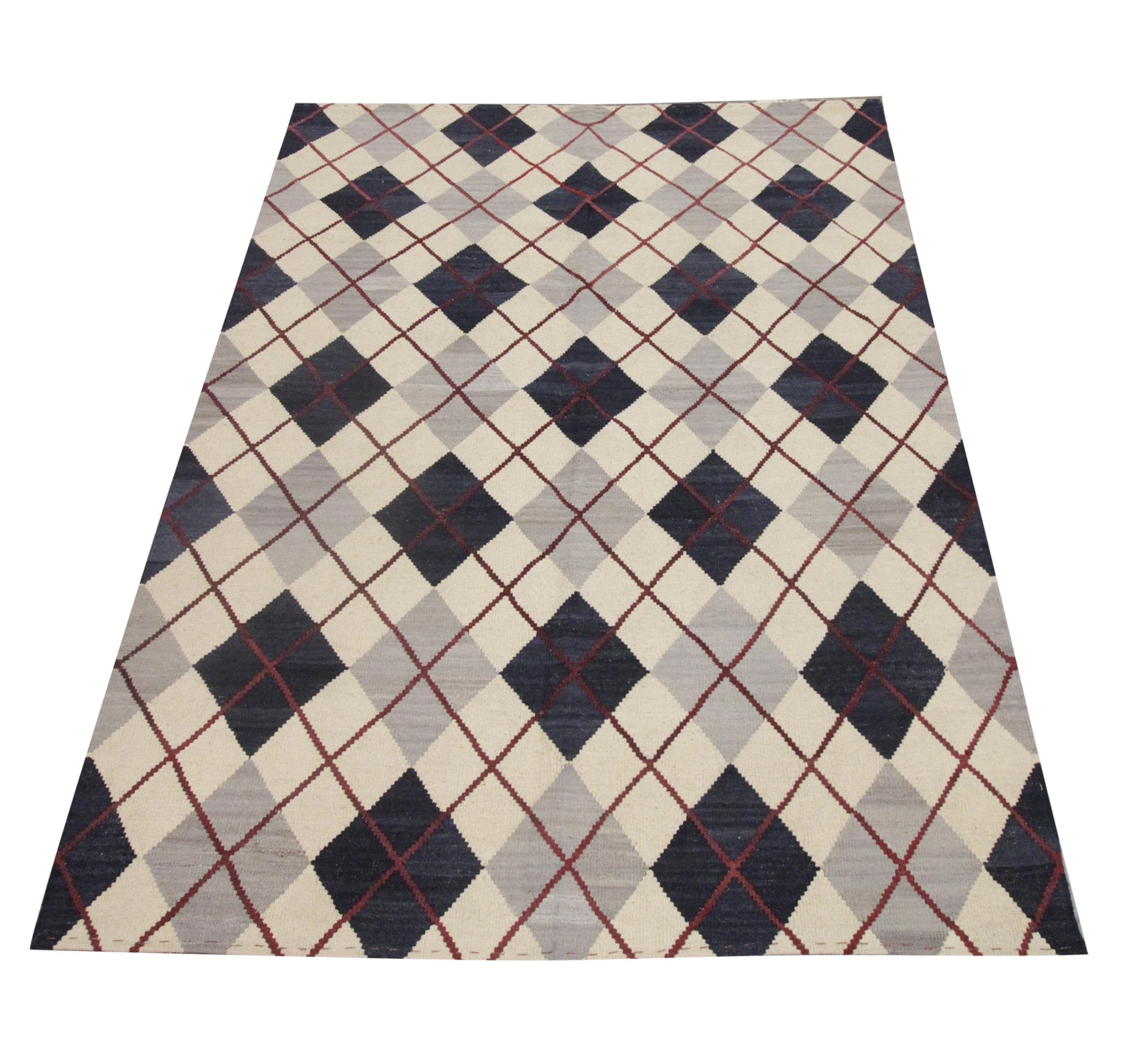 This fine wool Kilim is a handwoven area rug constructed in Afghanistan in the early 2000s. The design features a bold repeating geometric diamond pattern woven in grey, blue, and red accents on a simple cream background. The elegantly modern design