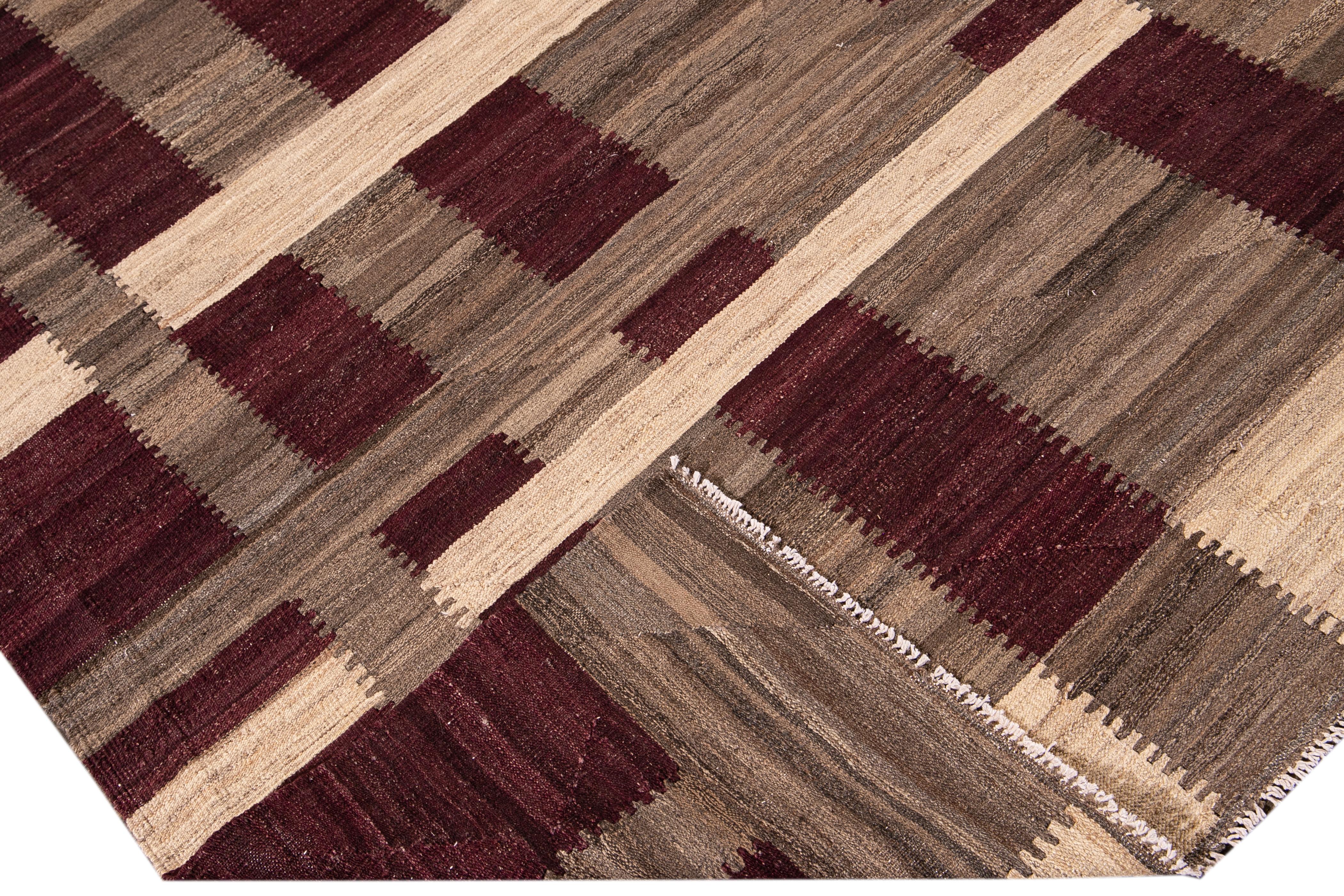 Beautiful modern Kilim flat-weave wool rug with a beige and brown field. This piece of art has burgundy accents in a gorgeous geometric check pattern design.

This rug measures: 8'5