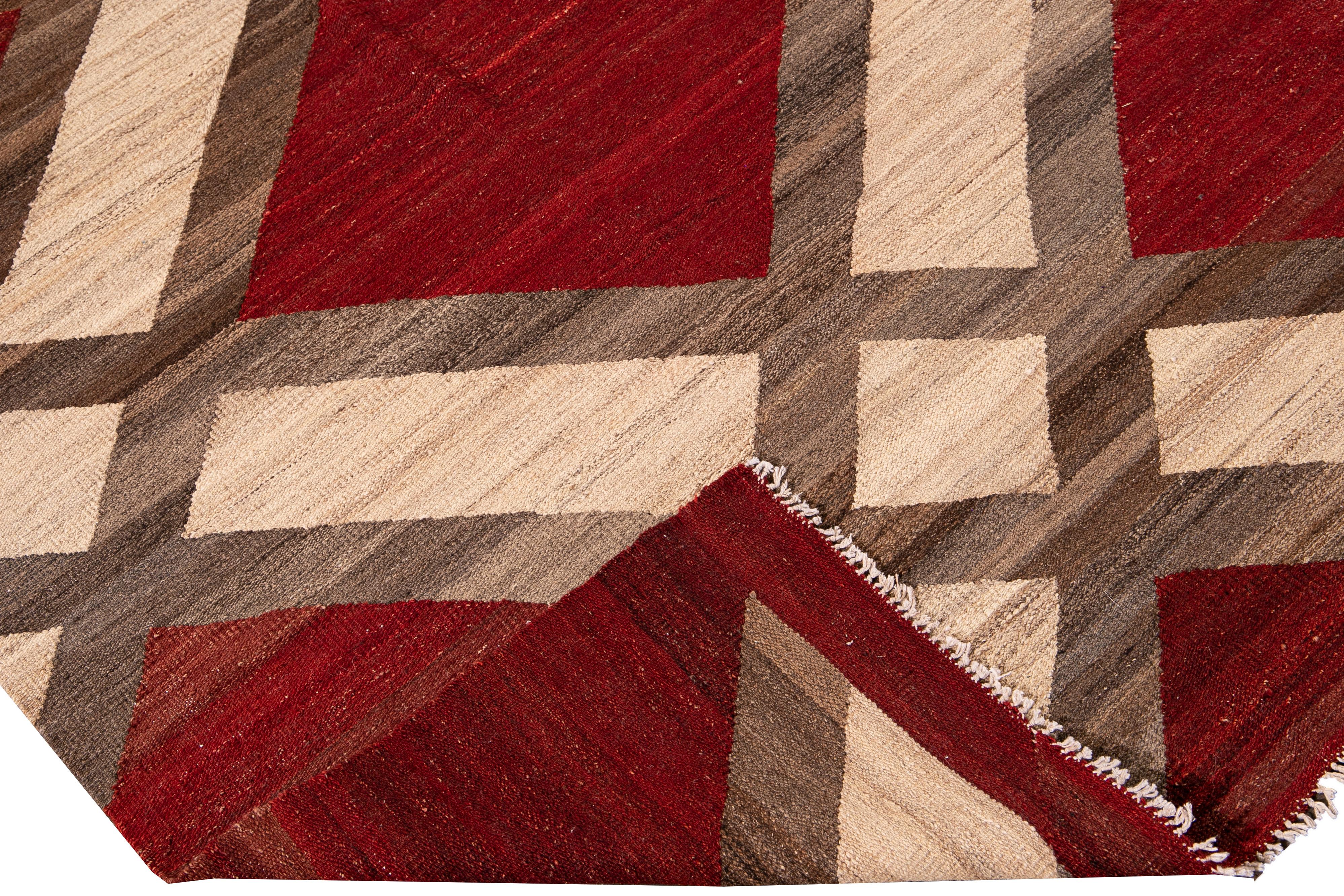 Beautiful modern Kilim flat-weave wool rug with a red field. This piece of art has beige and brown accents in a gorgeous geometric pattern design.

This rug measures: 8'3