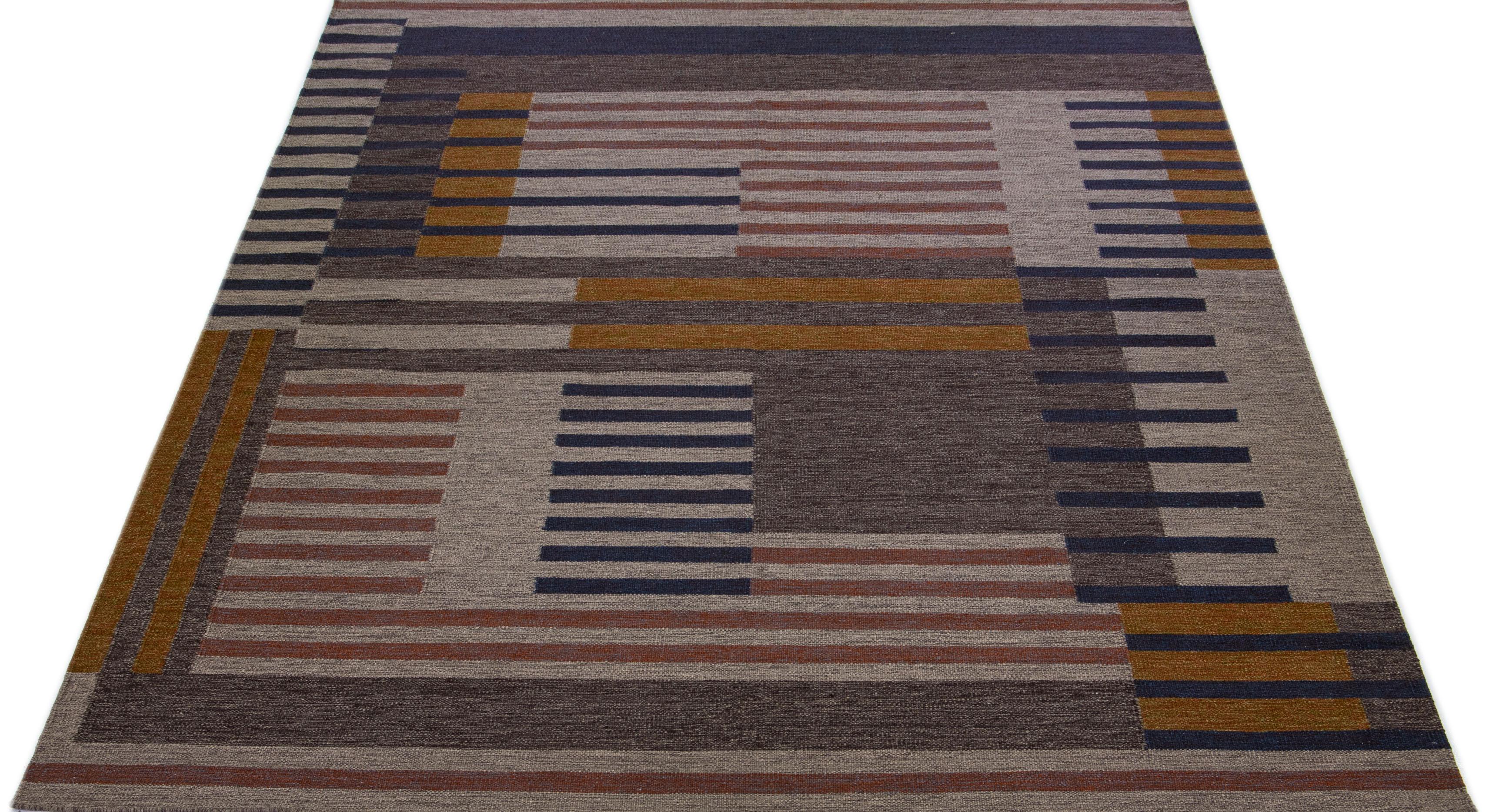 Esta exquisita alfombra india muestra un espléndido estilo Kilim contemporáneo de tejido plano, elaborado con lana de primera calidad. Su combinación de colores beige y marrón emana elegancia, complementada por un cautivador dibujo geométrico que