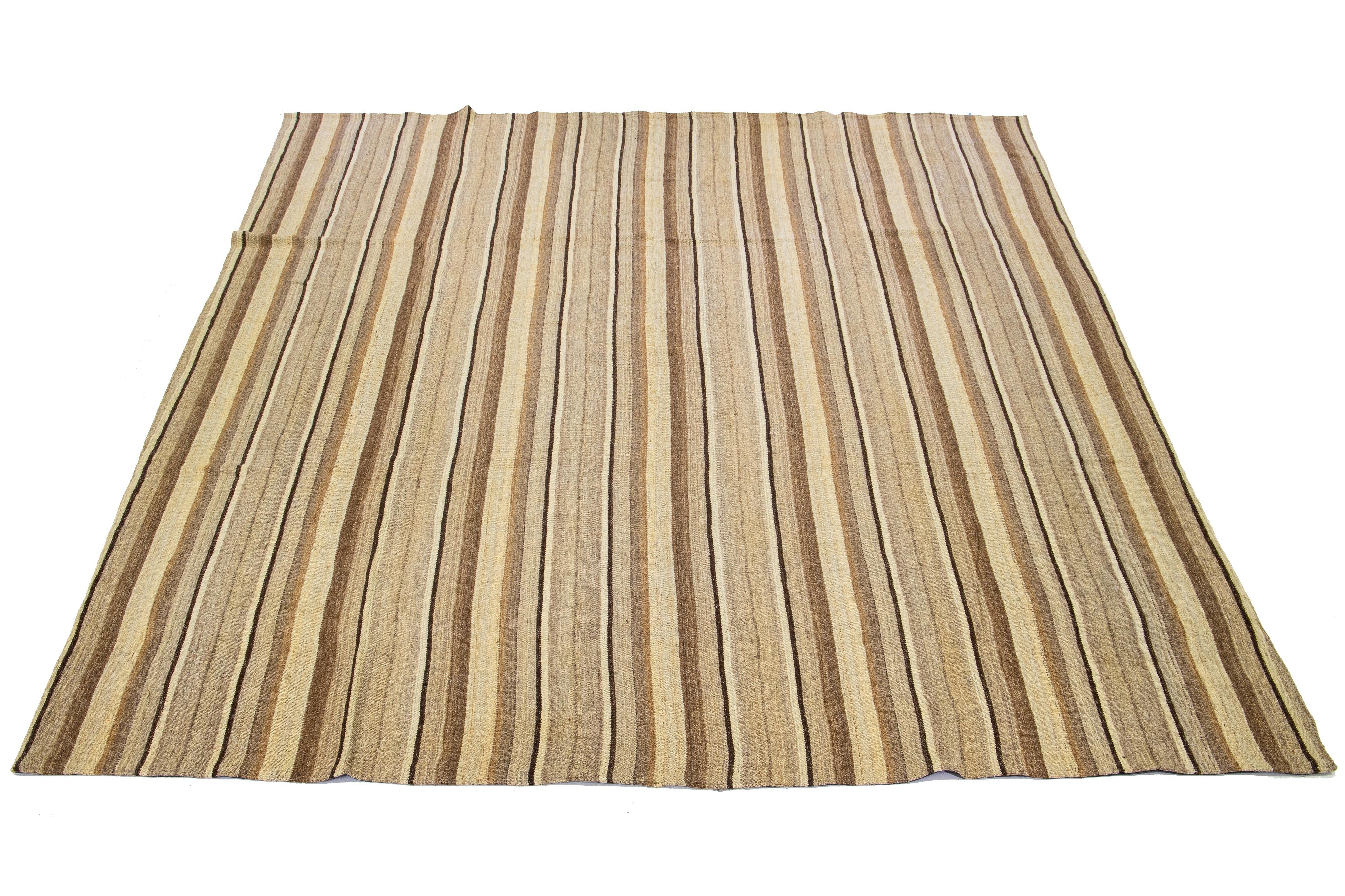 This Indian rug showcases a contemporary Kilim flatweave style crafted from wool. The rug exhibits an elegant striped pattern in shades of beige and brown.

This rug measures 10'9