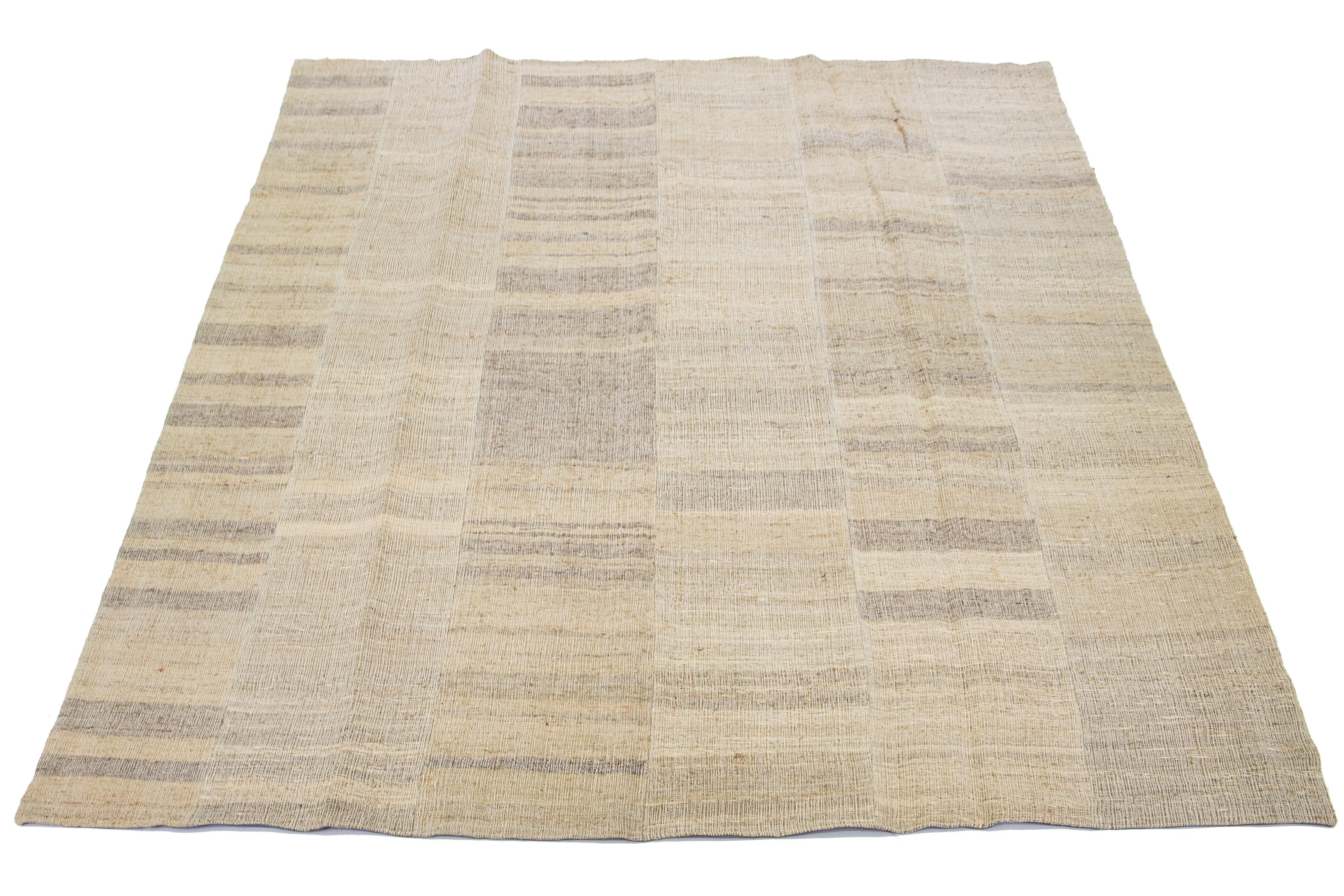 This Indian rug showcases a contemporary Kilim flatweave style crafted from wool. The rug has a beige field with a striped pattern in brown shades.

This rug measures 9'11