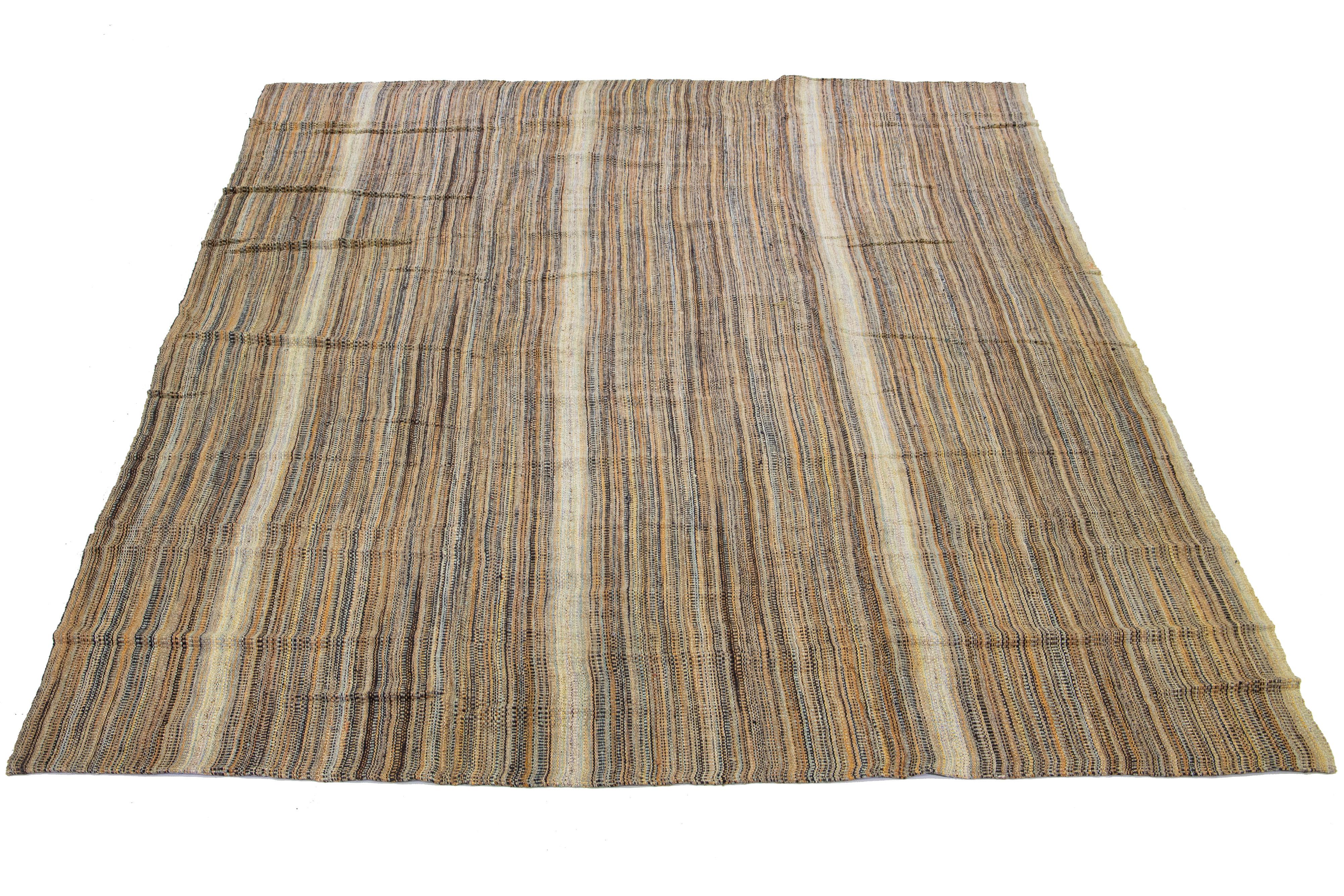 This Indian rug showcases a contemporary Kilim flatweave style crafted from wool. The rug exhibits an elegant striped pattern in beige, tan, and brown shades.

This rug measures 11'8