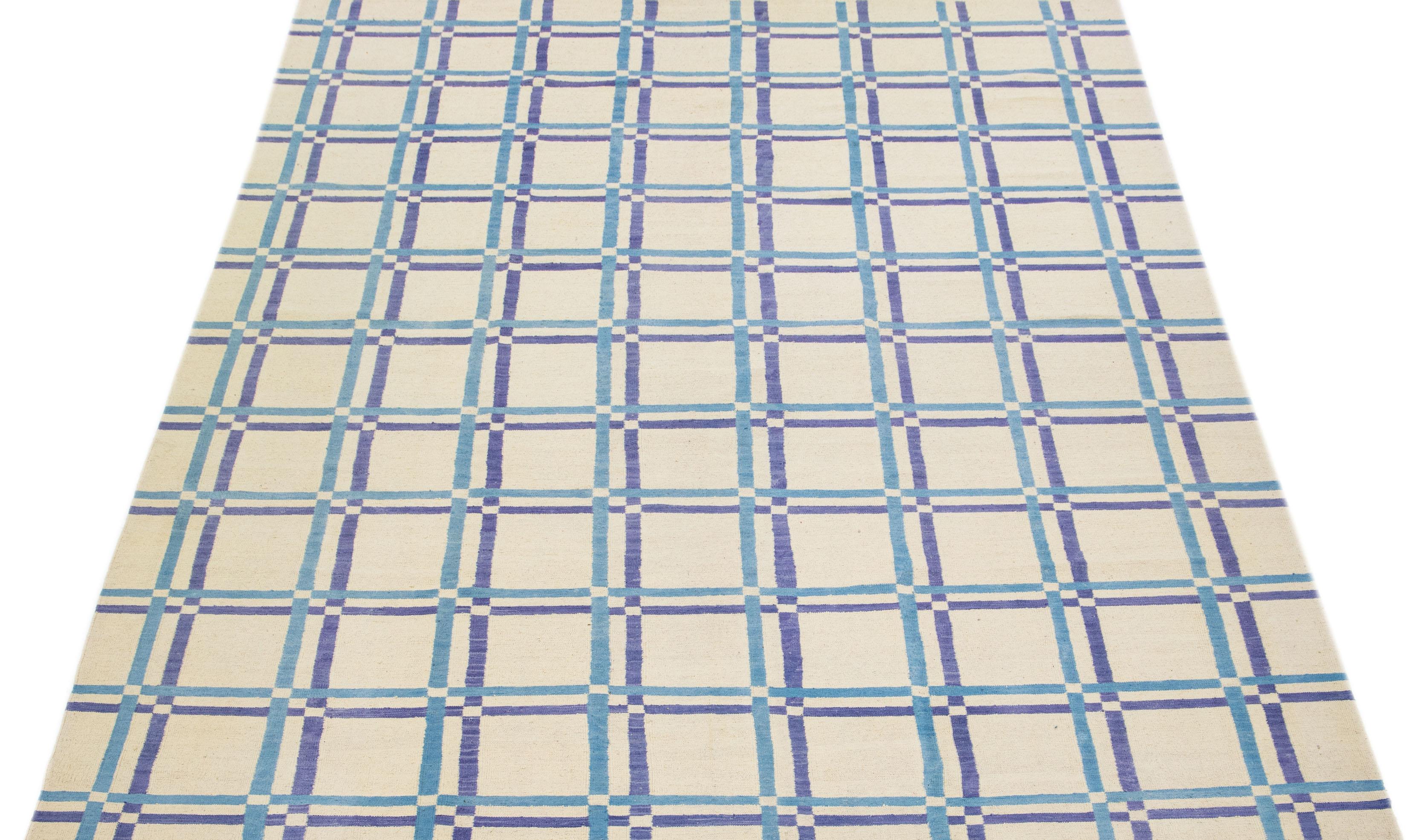 Ce tapis moderne Rug & Kilim respire l'élégance avec sa laine finement tissée à plat, présentée dans une captivante teinte ivoire complétée par un étonnant motif géométrique aux accents bleus.

Ce tapis mesure 9'2