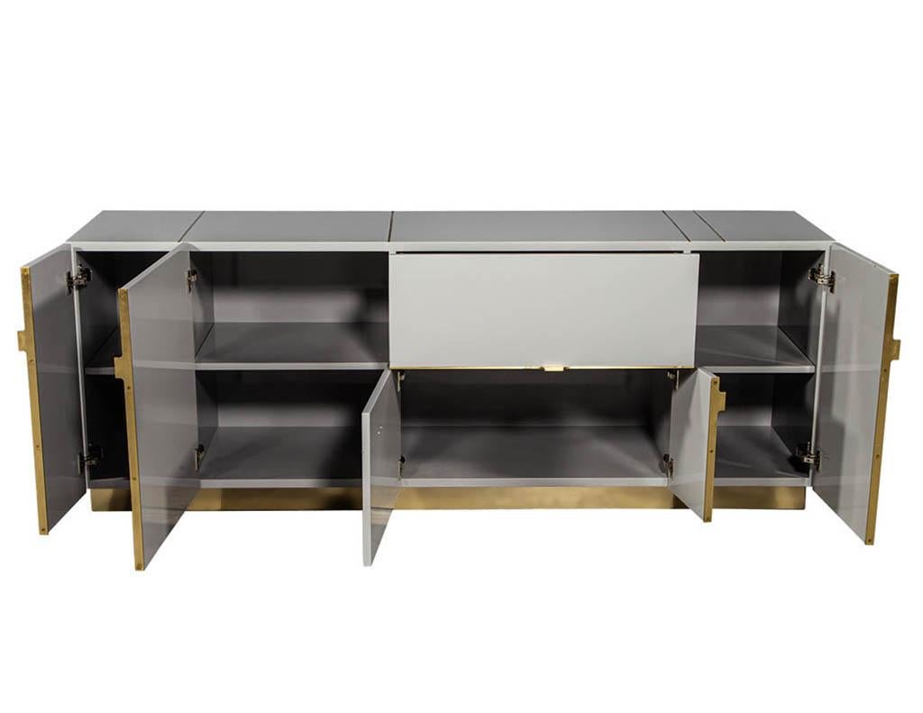 Modern lacquered buffet credenza sideboard with brass detail. Modern custom design credenza with solid brass detailing and platform base. Finished in a hand polished dove grey lacquer.

Price includes complementary curb side delivery to the