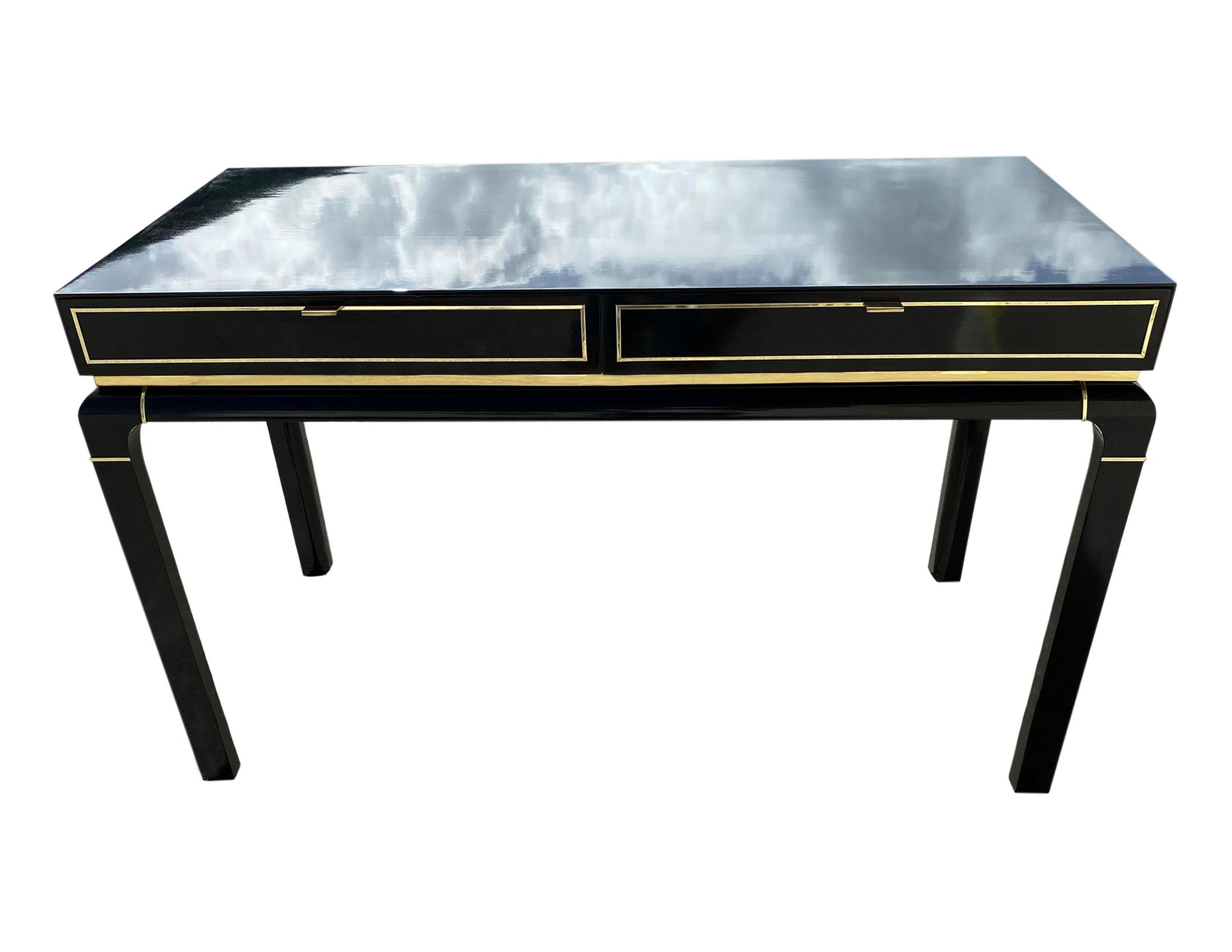 A timeless vintage piece, this midcentury writing desk feels glamourous, manufactured for John Stuart Inc. Adorning its exterior of glossy black lacquer, paired with bright brass accents feels crisp and luxe. Two spacious drawers for storage. This