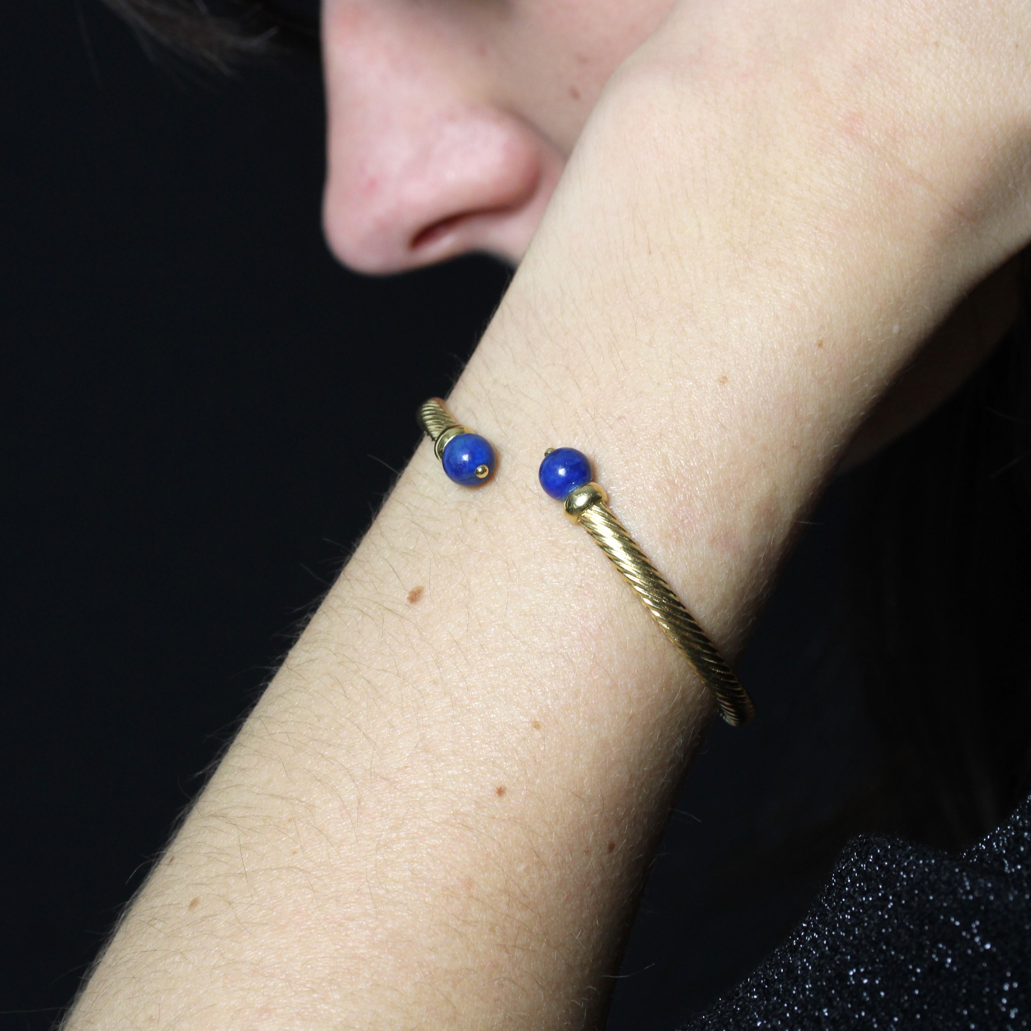 Bracelet en or jaune 18 carats, poinçon tête d'aigle.
Bracelet d'occasion en or jaune, il est de forme ovale, ouvert aux extrémités et formé d'une torsade en or. Chaque extrémité est ornée d'une perle de lapis-lazuli.
Diamètre du lapis-lazuli : 7 mm