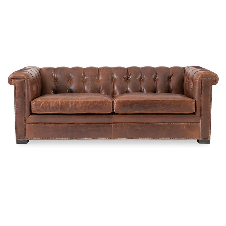 A Modern leather Chesterfield sofa. A take on the traditional 19th century English design with squared arms and backrest. 

The arms and backrest tufted with two comfort down seat cushions. Finished with brass nailhead details and raised on modern