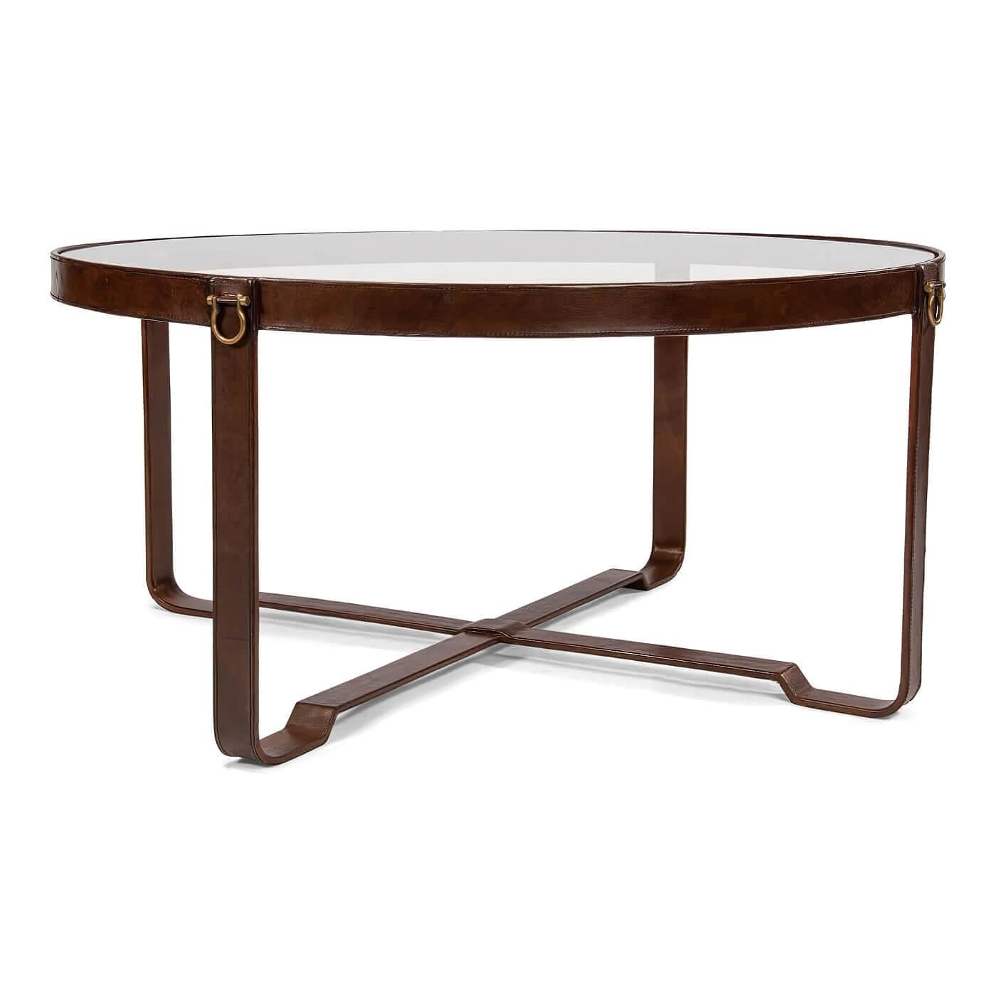 A modern leather-wrapped glass top round coffee table. The sleek glass top sits on metal legs covered in antique leather with brass details. The brass details on the sides give this piece an equestrian feel. 

Dimensions: 40