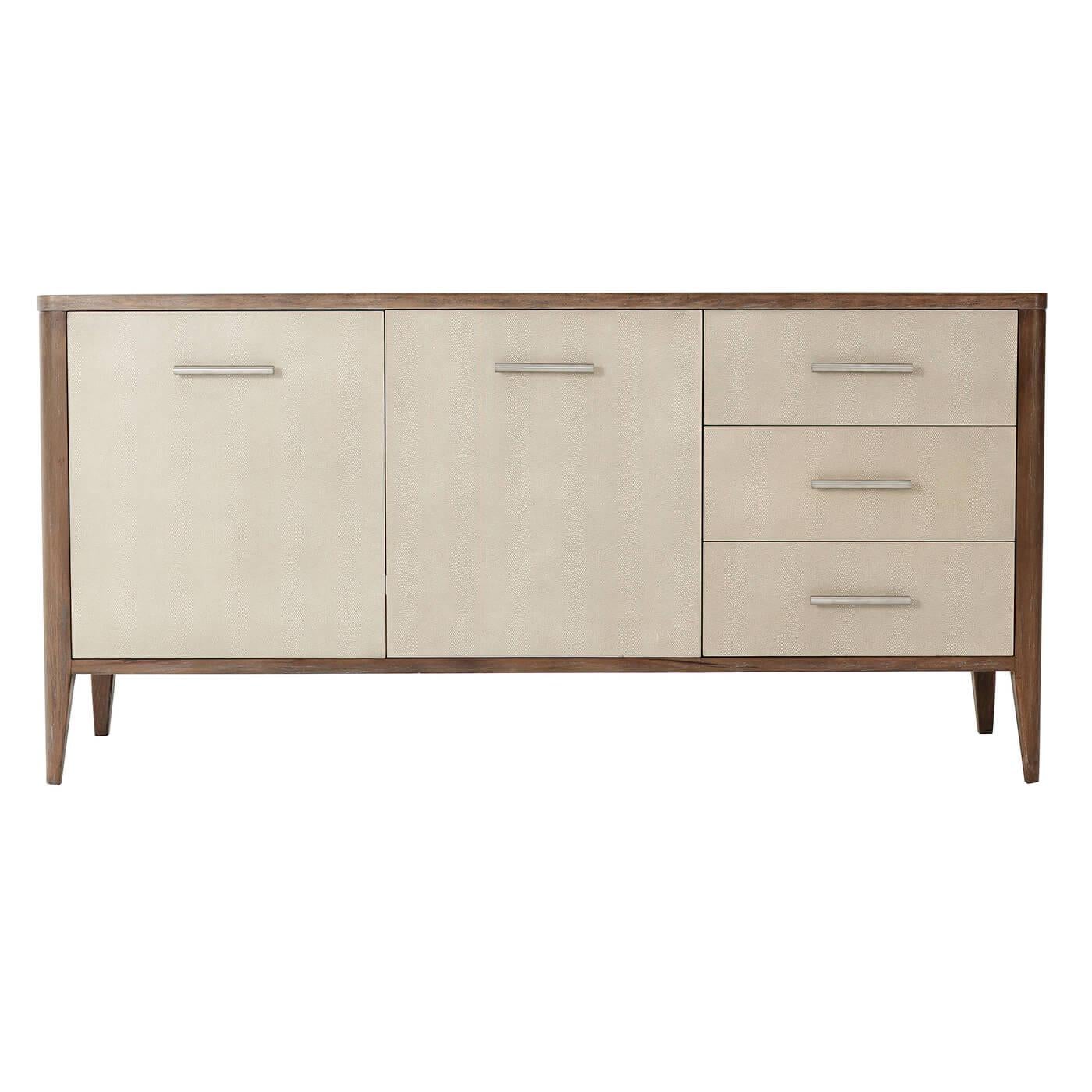 Midcentury style Komodo embossed leather wrapped sideboard with mangrove finish primavera veneer and beech with three drawers beside a two-door cabinet enclosing adjustable shelved and with brushed brass finish handles.

Dimensions: 66.5