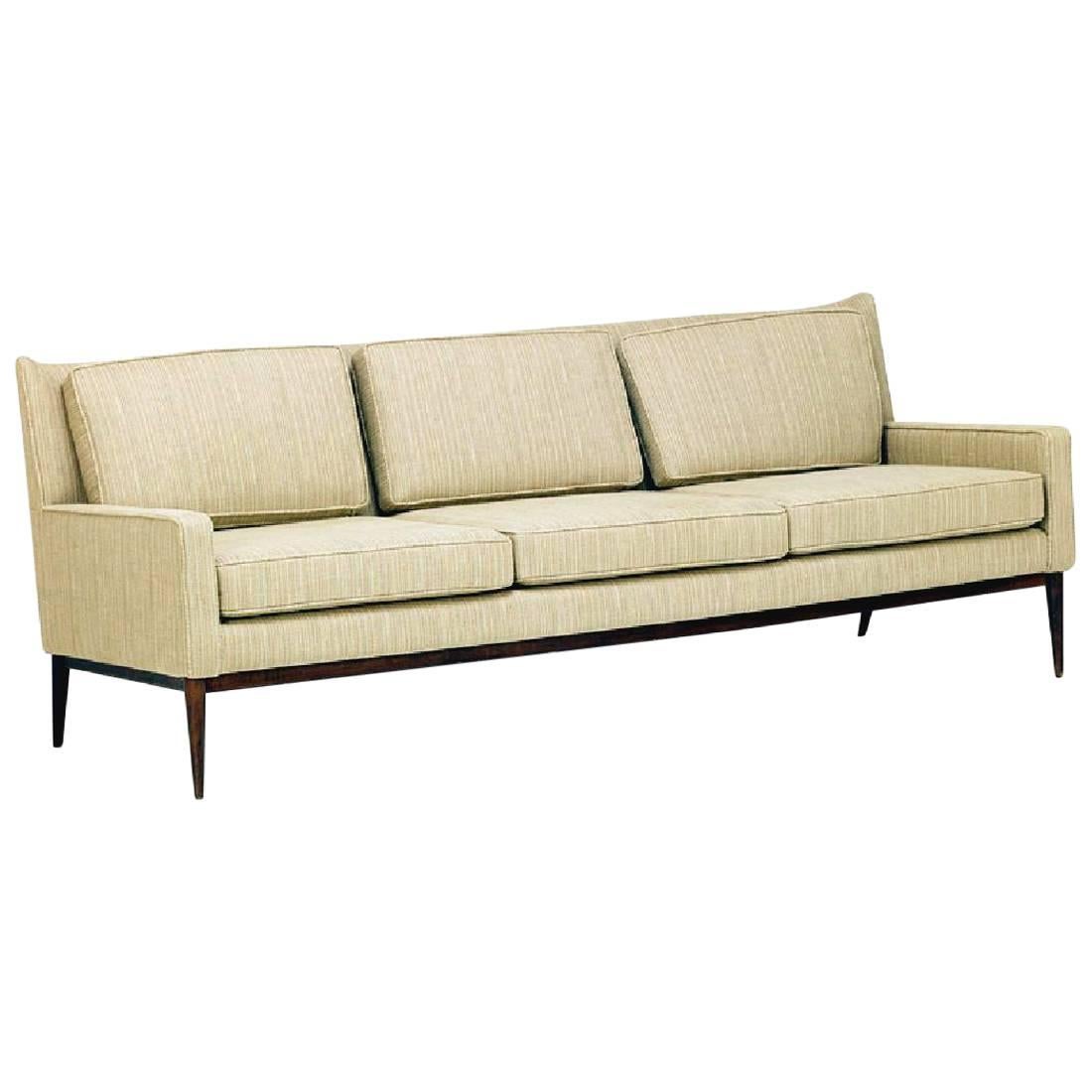 A midcentury three-seat sofa by Paul McCobb for Directional, model 1301. A very clean look with a slight wing back. It features three removable back and seat cushions on a conforming upholstered frame with dark wood base. Attractive 