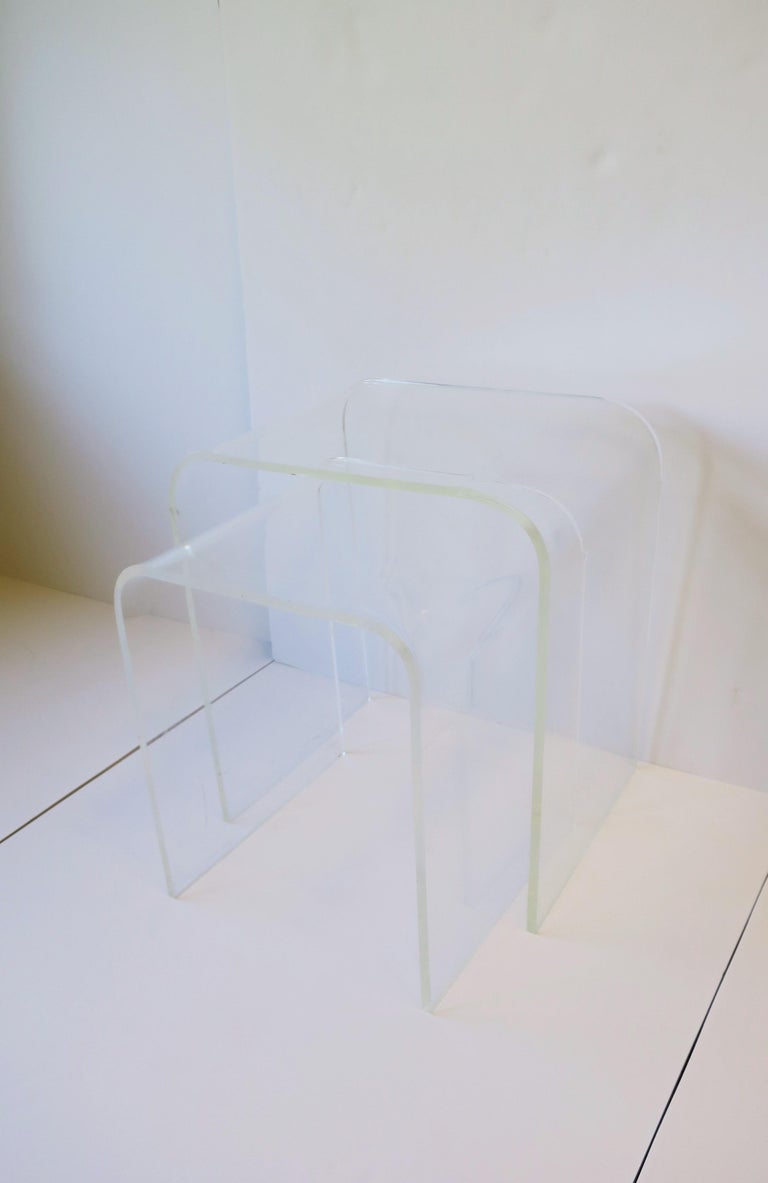 A set of (2) two Modern style Lucite nesting, end, or side tables with 'waterfall' edge, circa mid-20th century. These Modern style Lucite nesting table are versatile; set can work as small side/drinks tables or as an end table with 'pull' out side