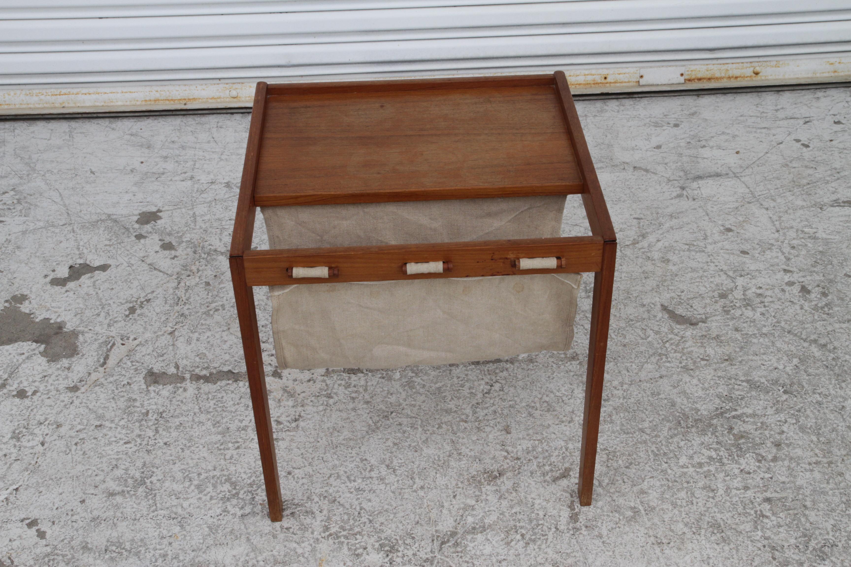  Modern table features solid teak construction with canvas sling magazine holder and tall tapered legs.
Dimensions: 18w 18d 18h

Condition: Original finish is in excellent condition with only minor scuffs, small scratches, slight edge dings. There